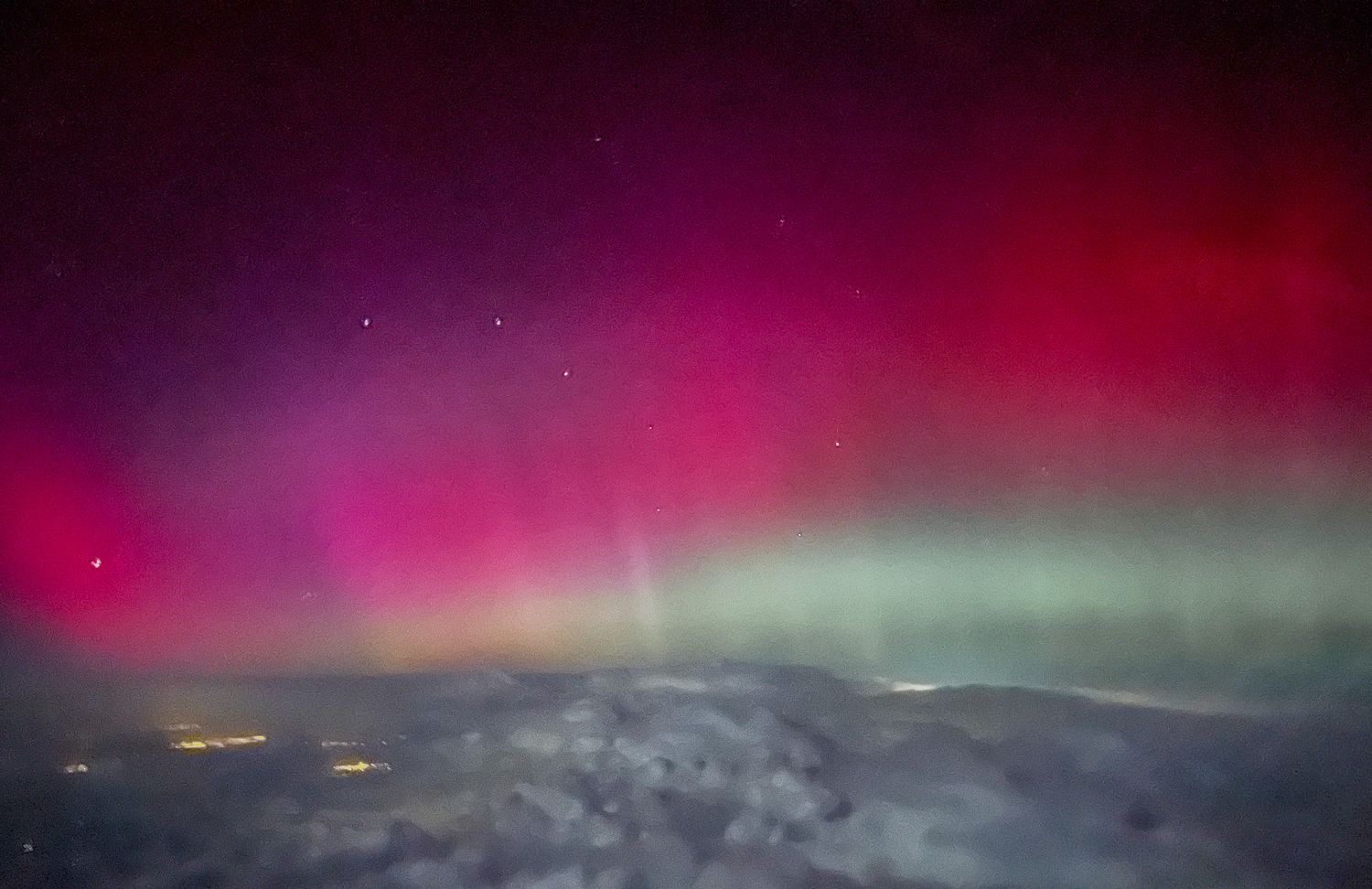 Breathtaking aurora borealis displaying vivid red and green northern lights viewed from an airplane window.