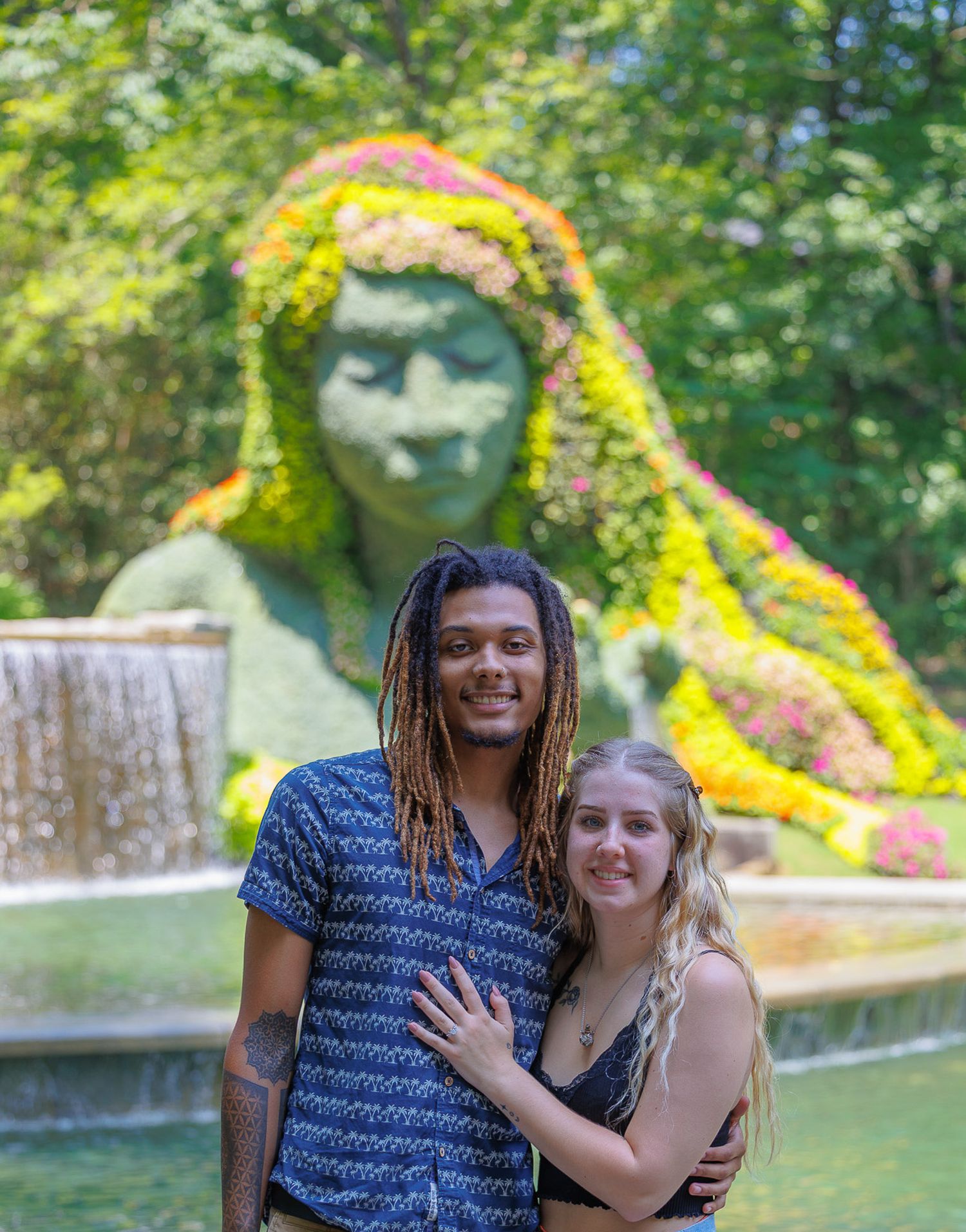 Engaged couple posing together in front of a large floral sculpture at a botanical garden.