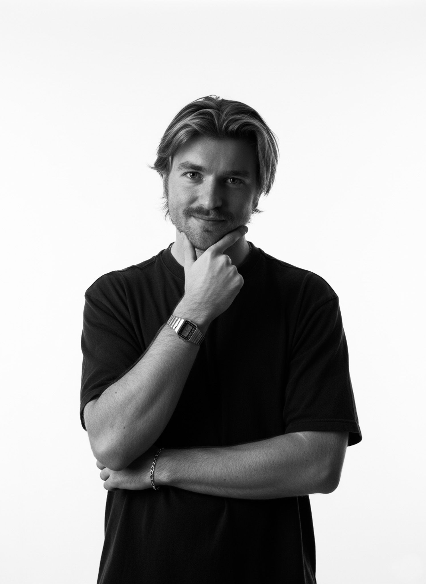 Black and white portrait of thoughtful man in black t-shirt with hand on chin against white background.