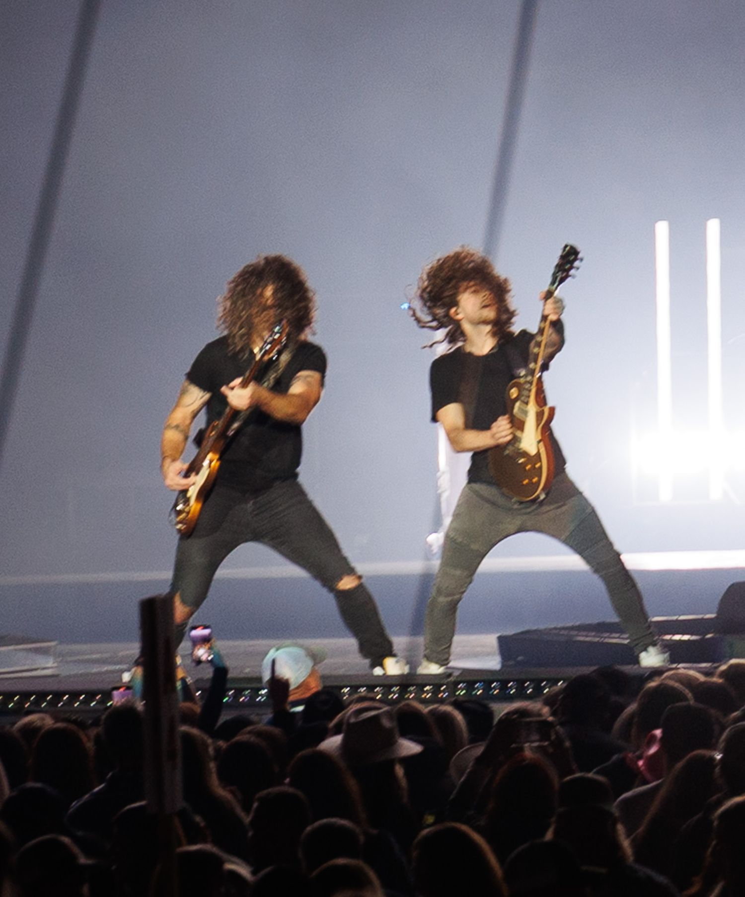 Two long-haired guitarists rock out together on stage with matching electric guitars at concert.