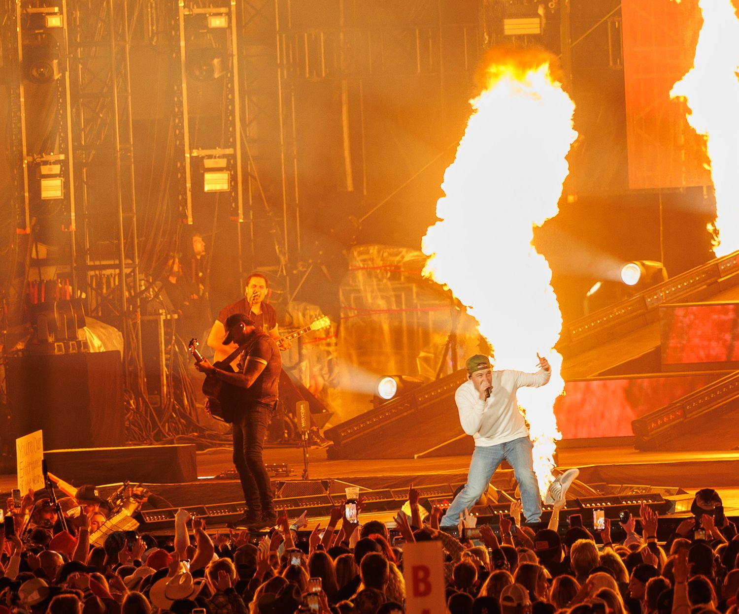 Two performers rock stage amid massive pyrotechnic fire explosions at high-energy concert.