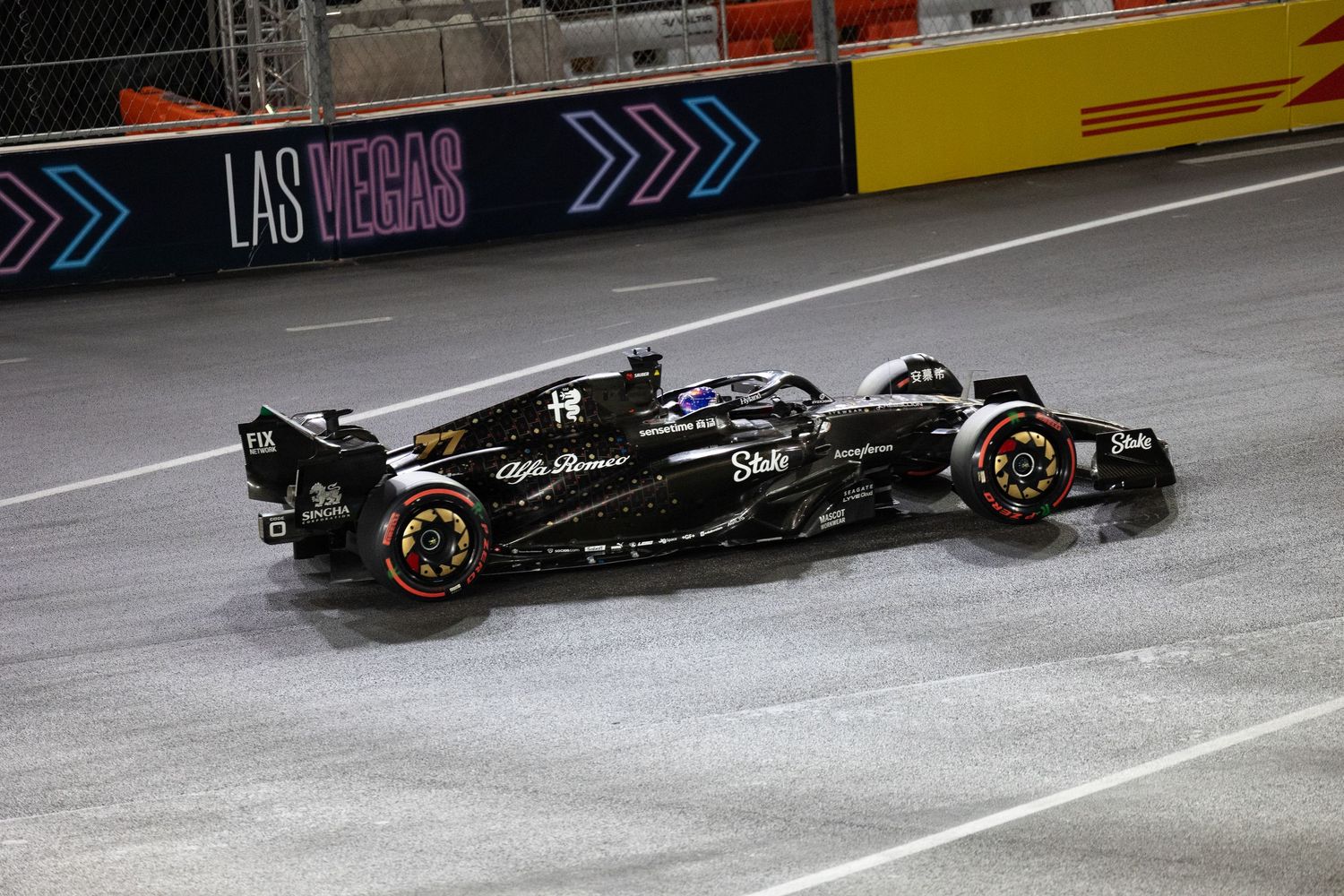 Alfa Romeo F1 car racing on wet Las Vegas Grand Prix street circuit at night.