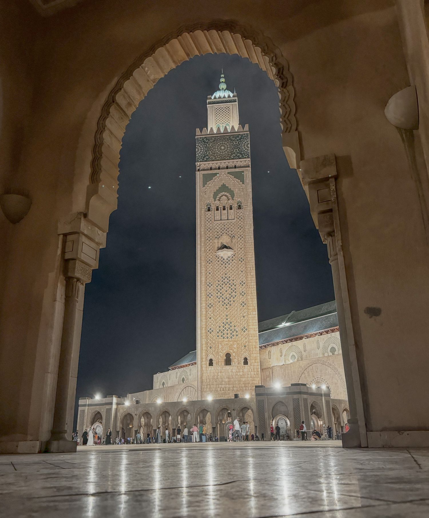 Hassan II Mosque minaret illuminated at night framed by ornate Moroccan archway in Casablanca.