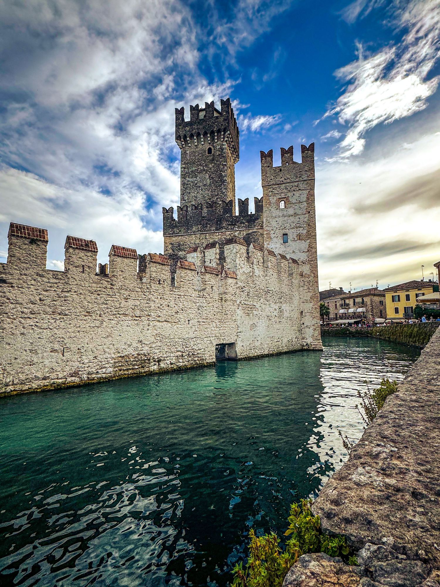 Medieval Scaligero Castle with turrets and stone walls reflected in turquoise waters of Lake Garda.