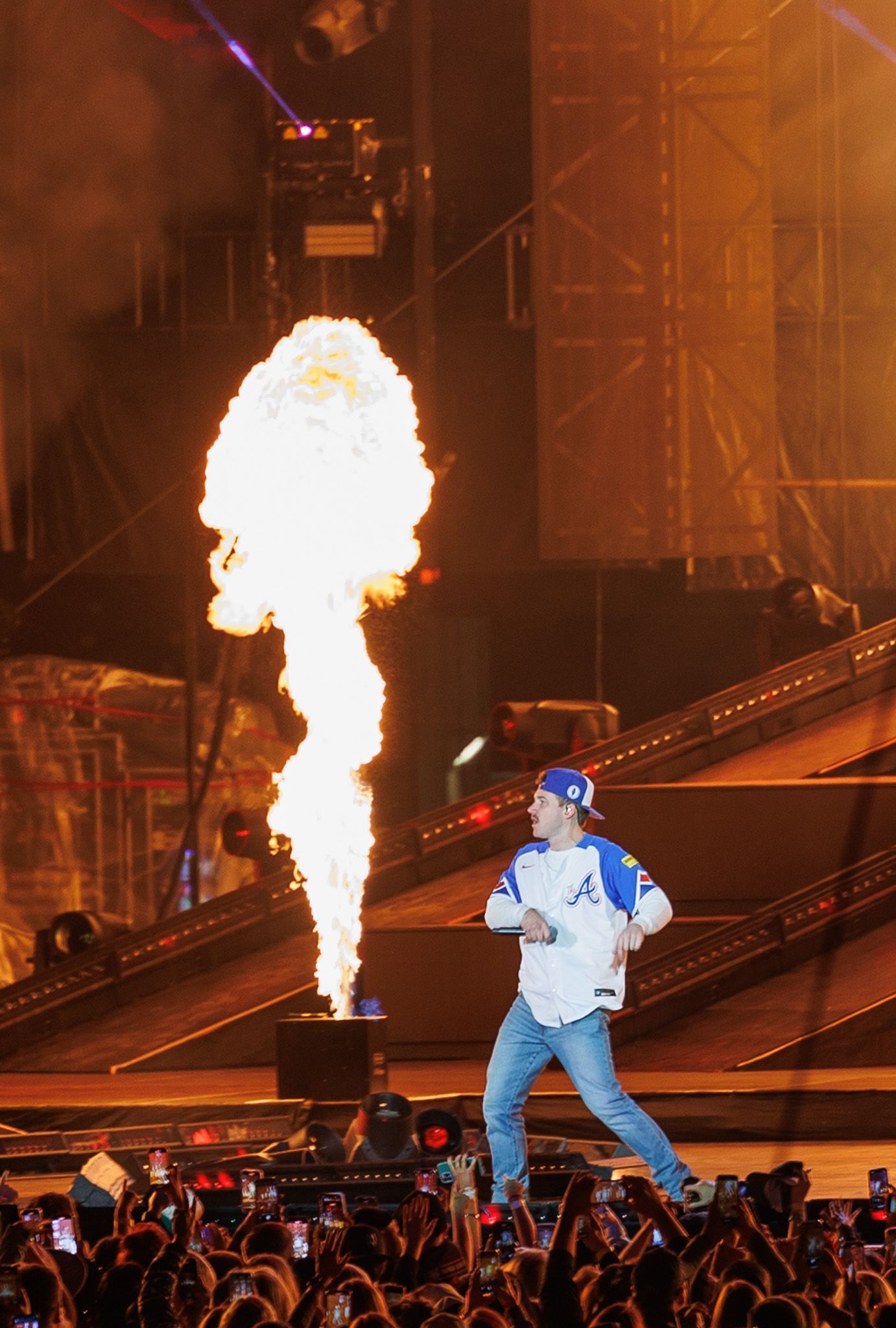 A performer in a Braves jersey walks on stage with a dramatic fire explosion behind him.