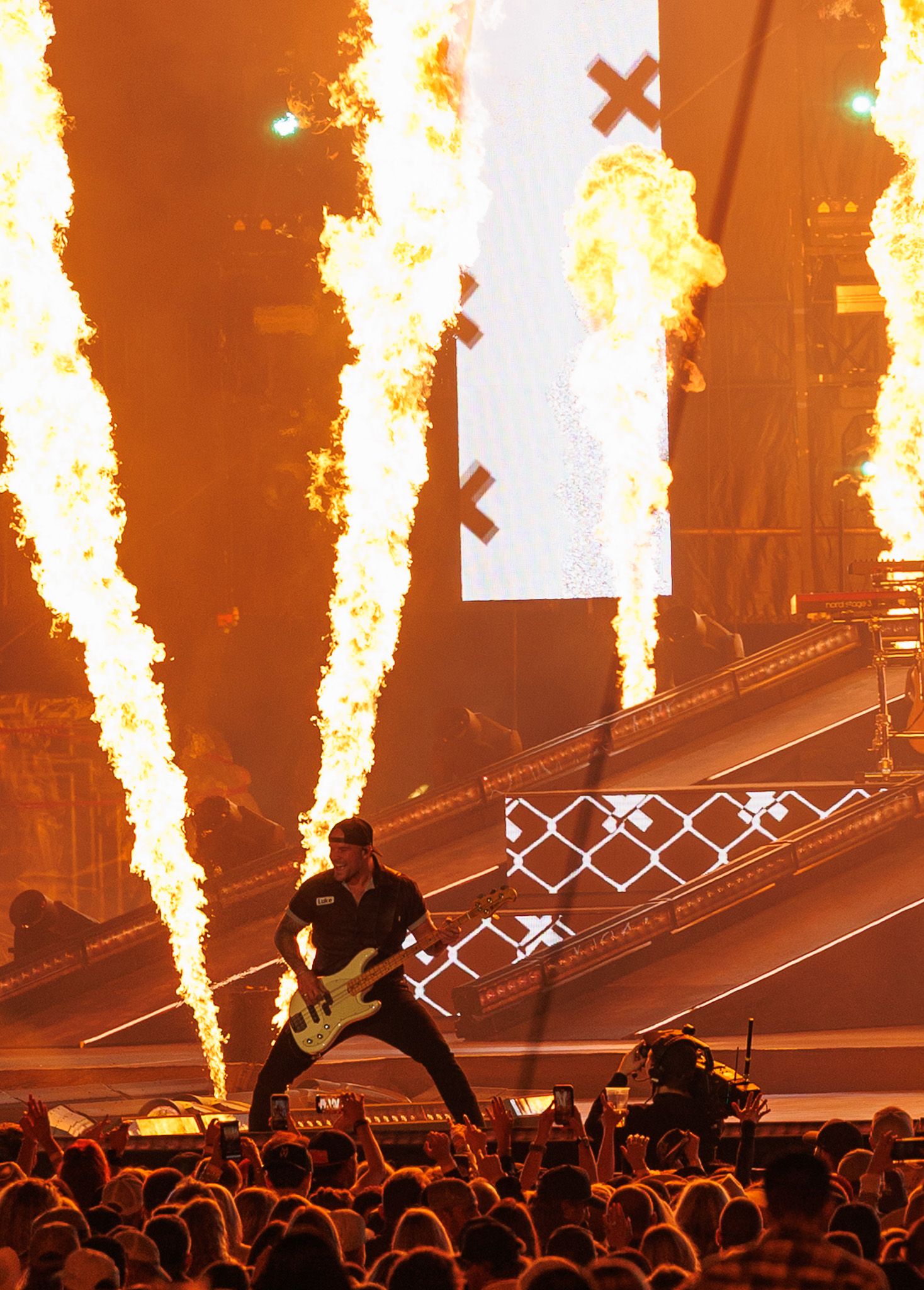 Rock guitarist performs on stage surrounded by massive pyrotechnic fire columns during an electrifying live concert.