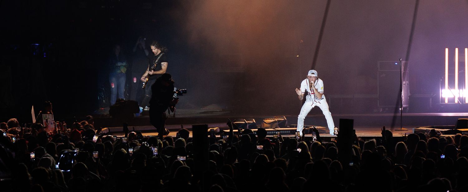 Two performers on darkened stage with dramatic backlighting entertain large arena crowd.