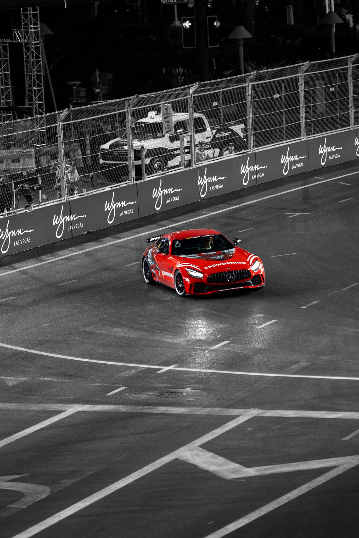 Red Mercedes-AMG GT racing on a wet street circuit track in selective color black and white photo.