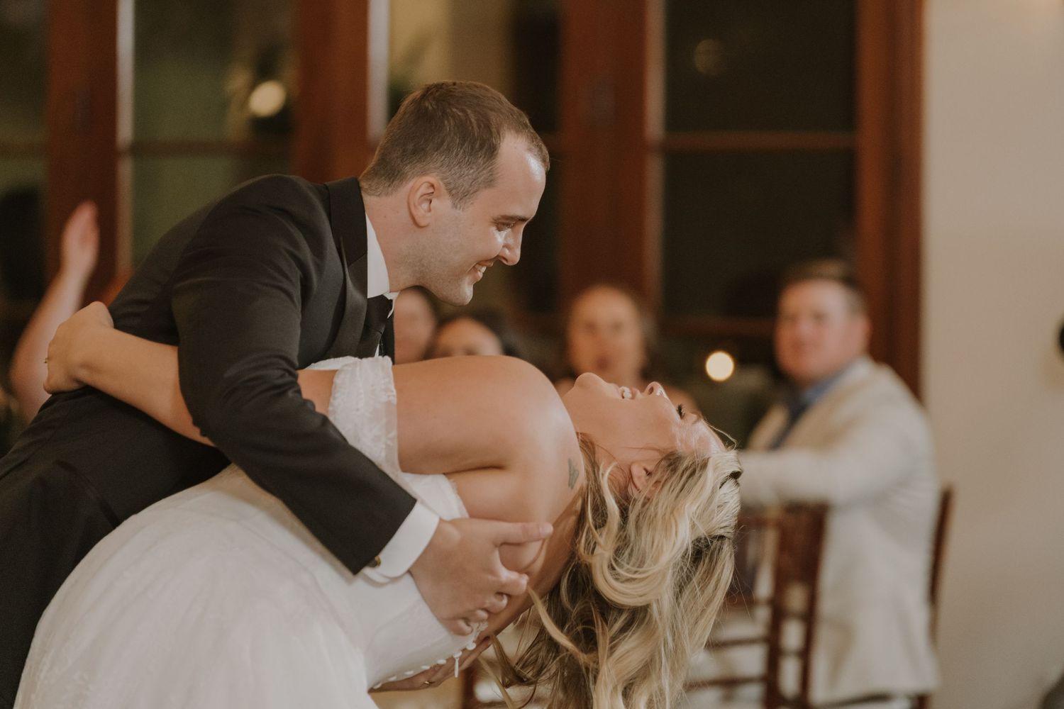 Groom dipping bride during romantic first dance at wedding reception with guests watching.