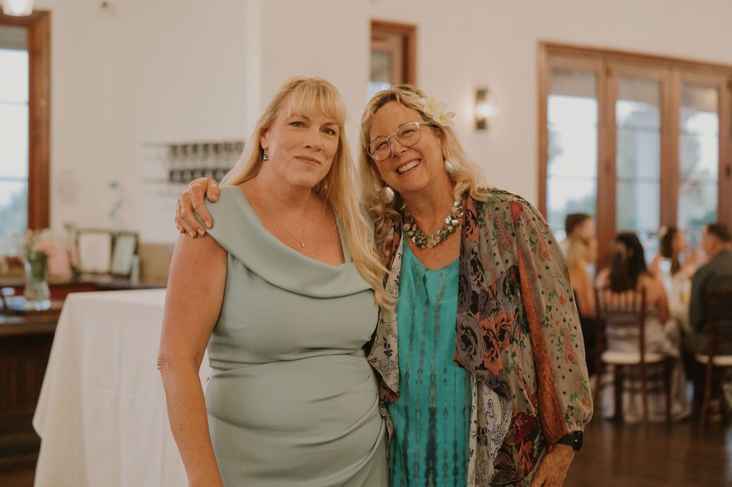 Two smiling women posing together at wedding reception in elegant venue.