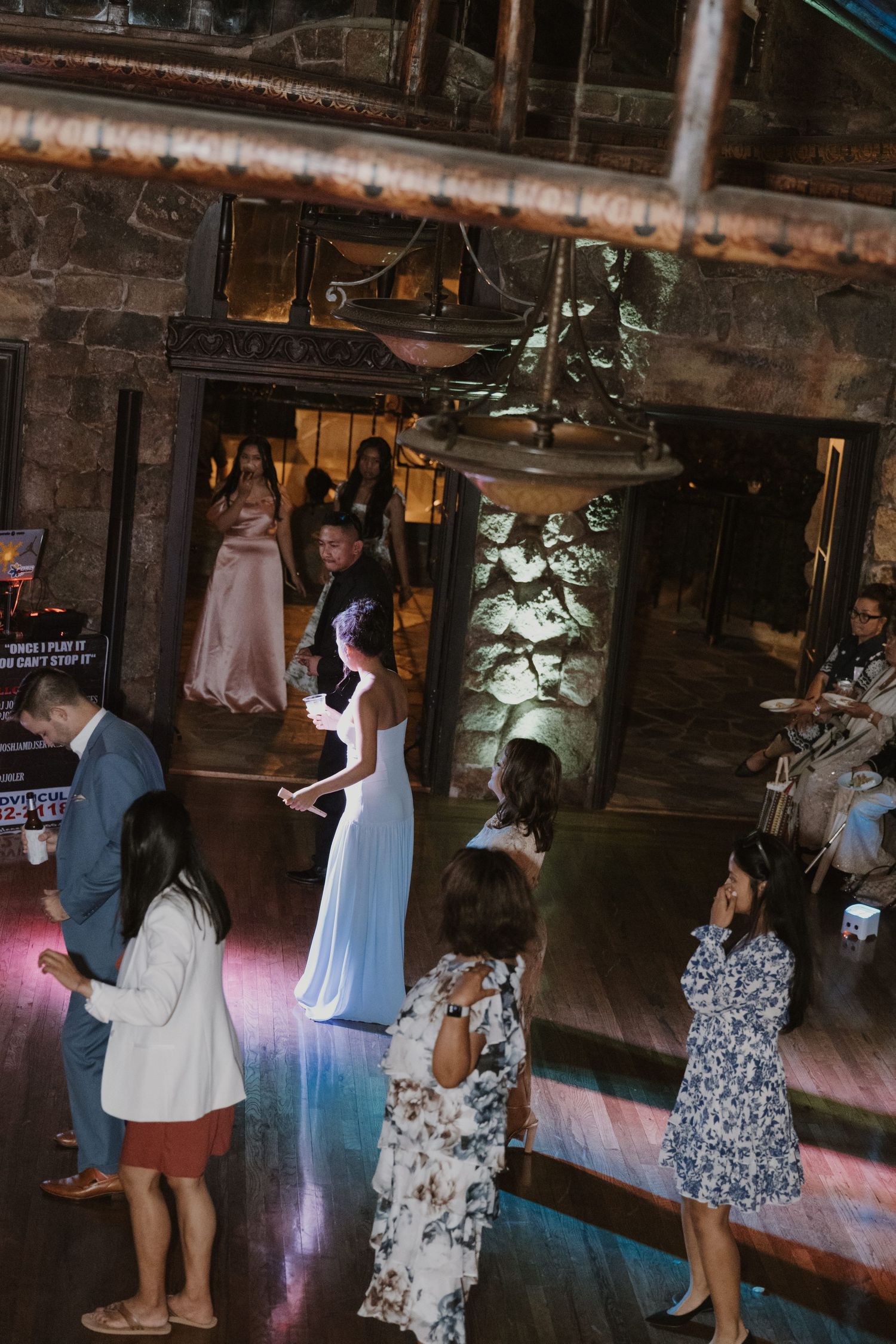 Bride in white gown dancing with guests in a rustic stone venue during a wedding reception celebration.