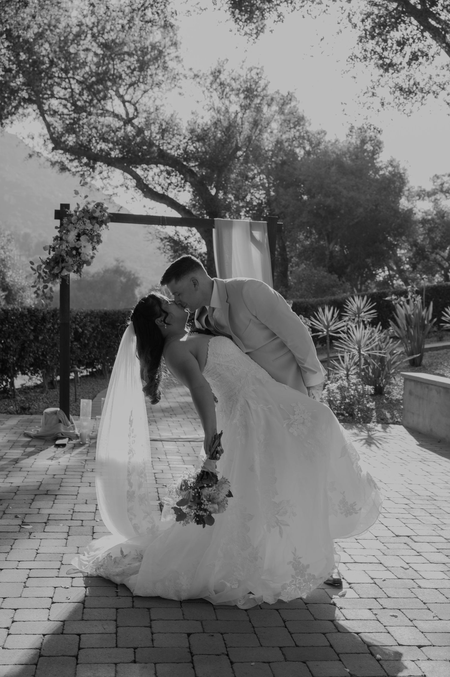 Groom dips bride for romantic kiss in wedding attire outdoors.