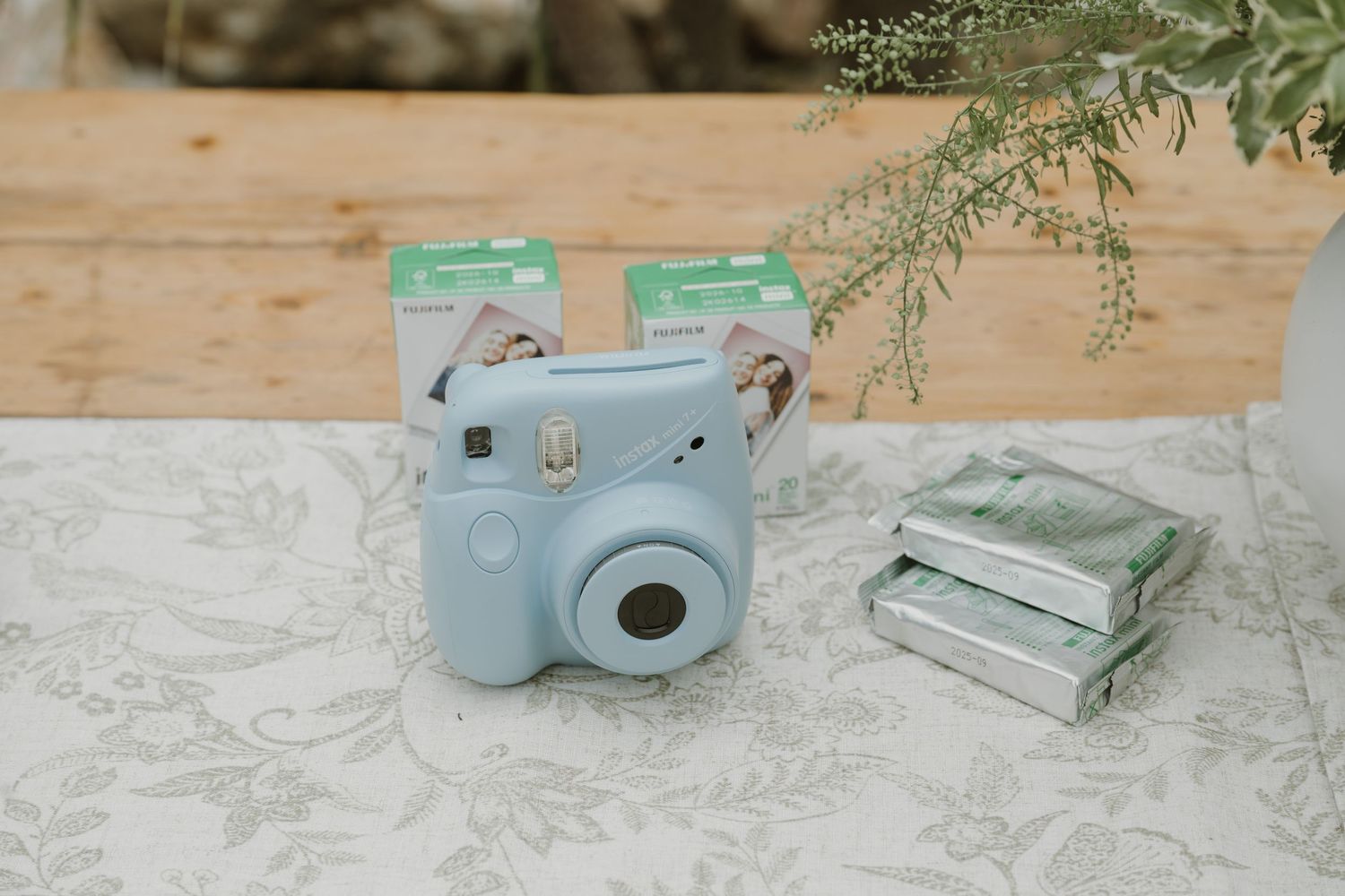 Light blue Fujifilm Instax Mini camera with film packs on a floral tablecloth at a wedding reception.