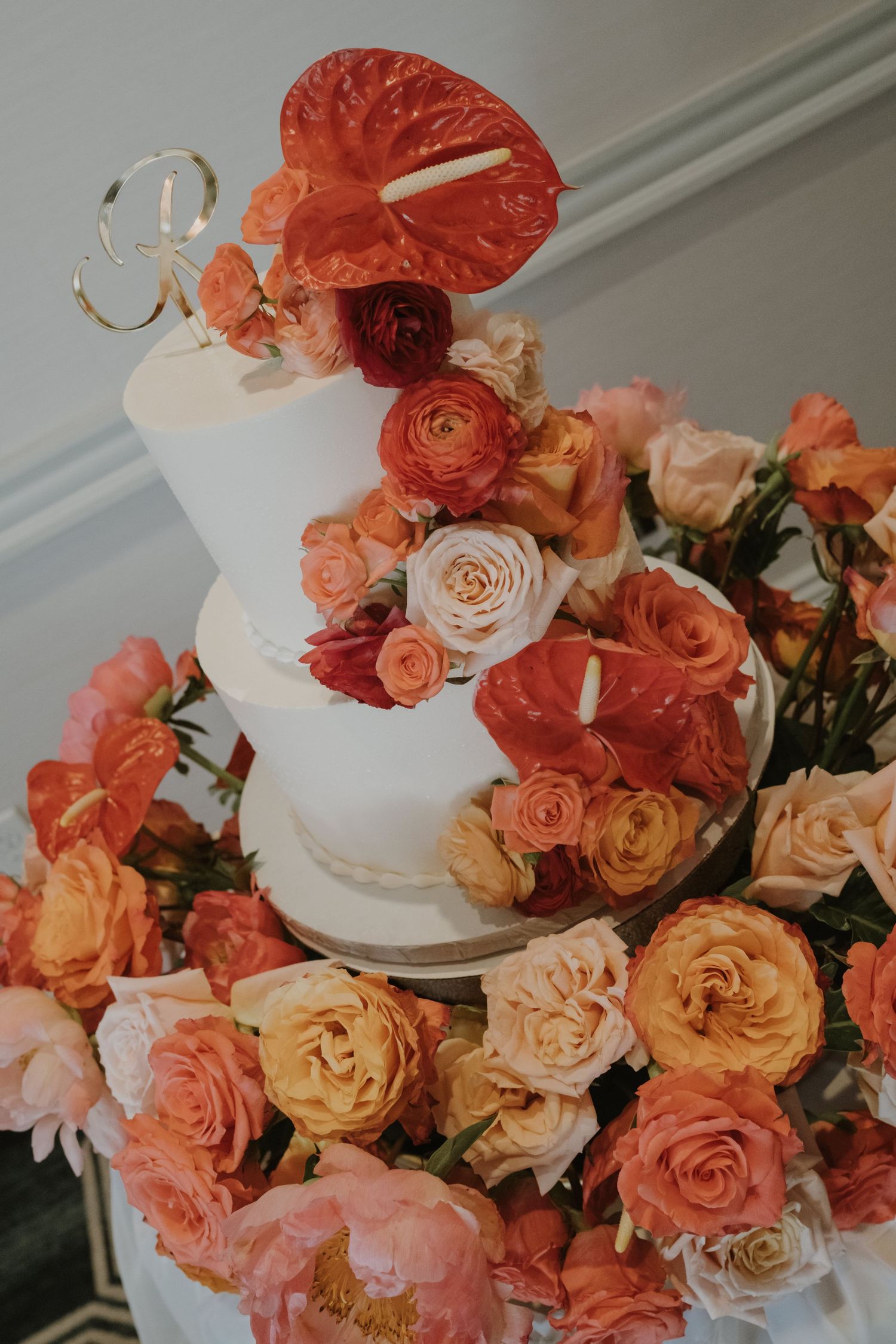 Three-tiered white wedding cake adorned with coral and peach roses.