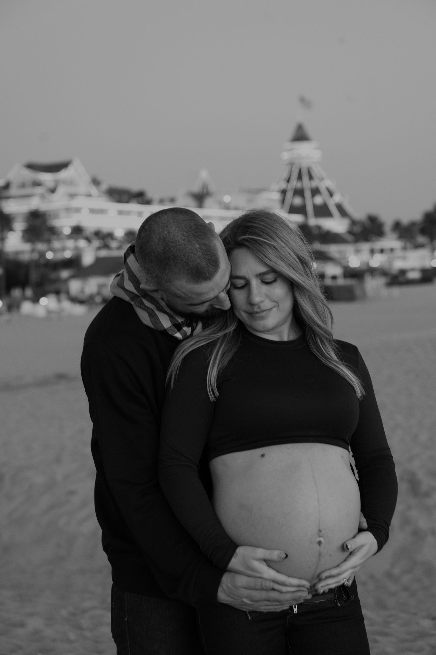Intimate maternity photoshoot on a beach with city skyline in background.