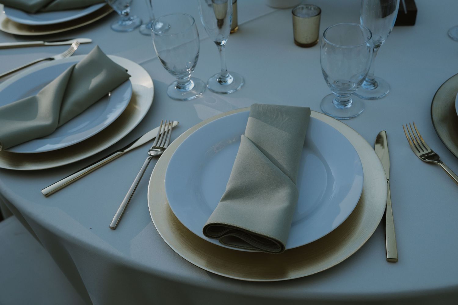 Close-up of formal place settings with white plates, silver cutlery, and folded napkins.