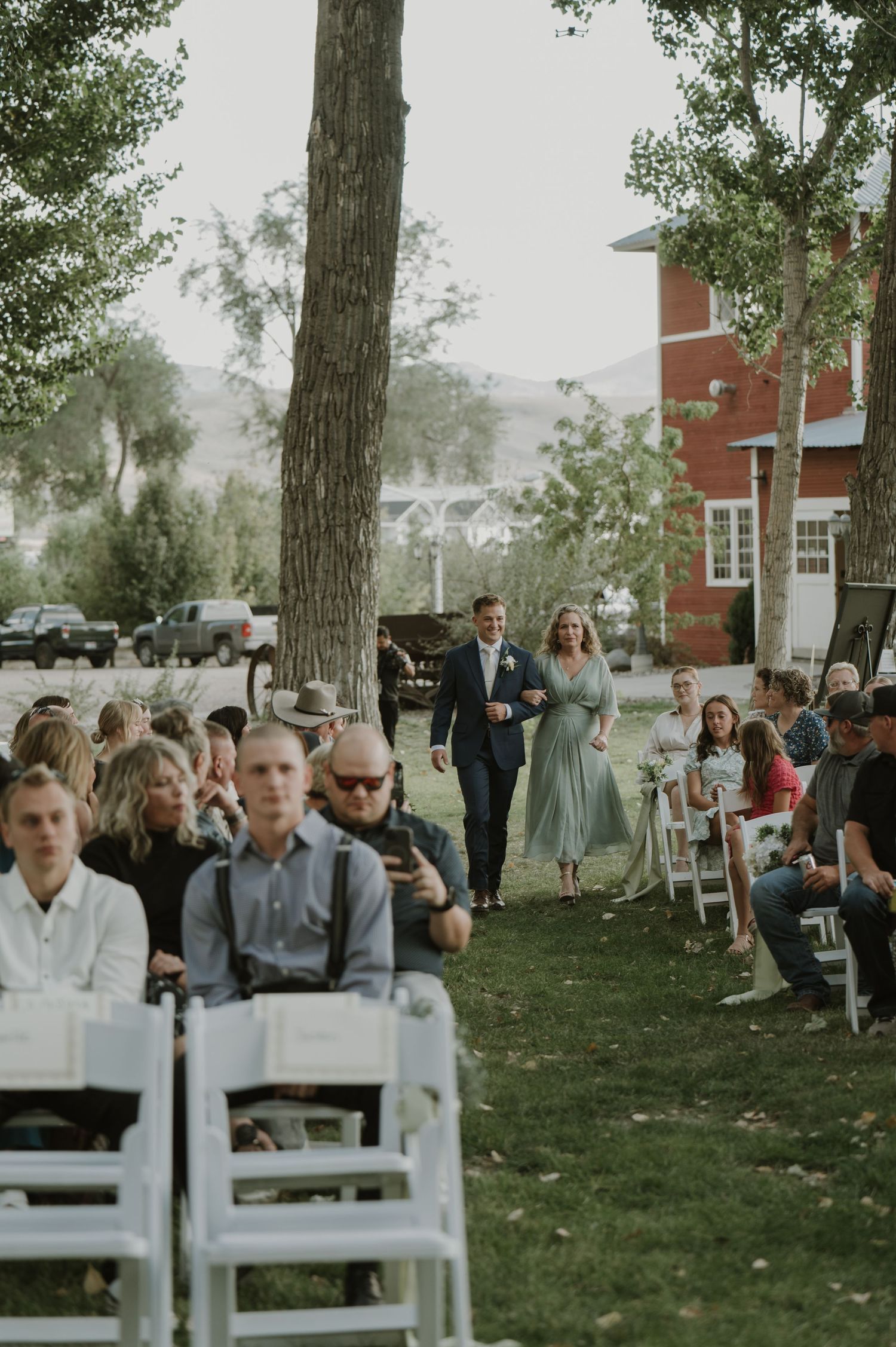 Outdoor wedding ceremony seating arrangement with white chairs set up under mature trees.