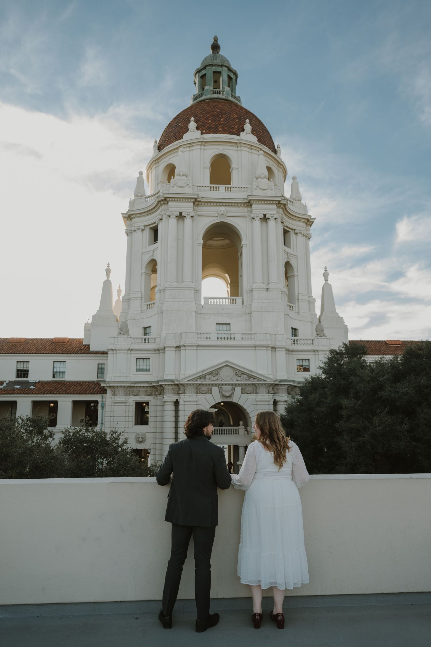 A couple stands together viewing a majestic white domed building against a blue sky.