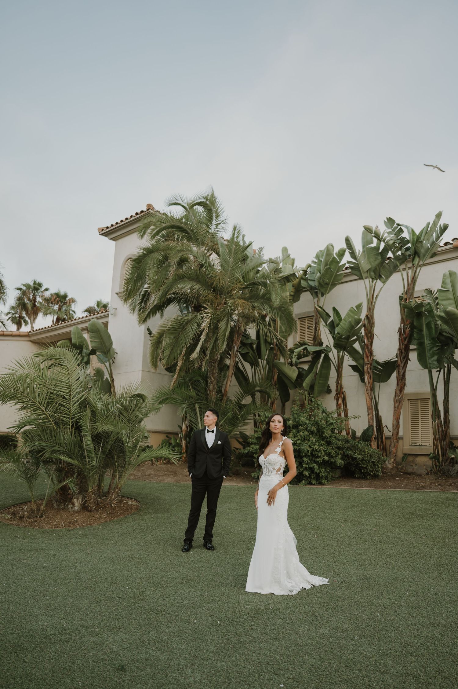 A tropical wedding photoshoot with palm trees and Spanish architecture in the background.