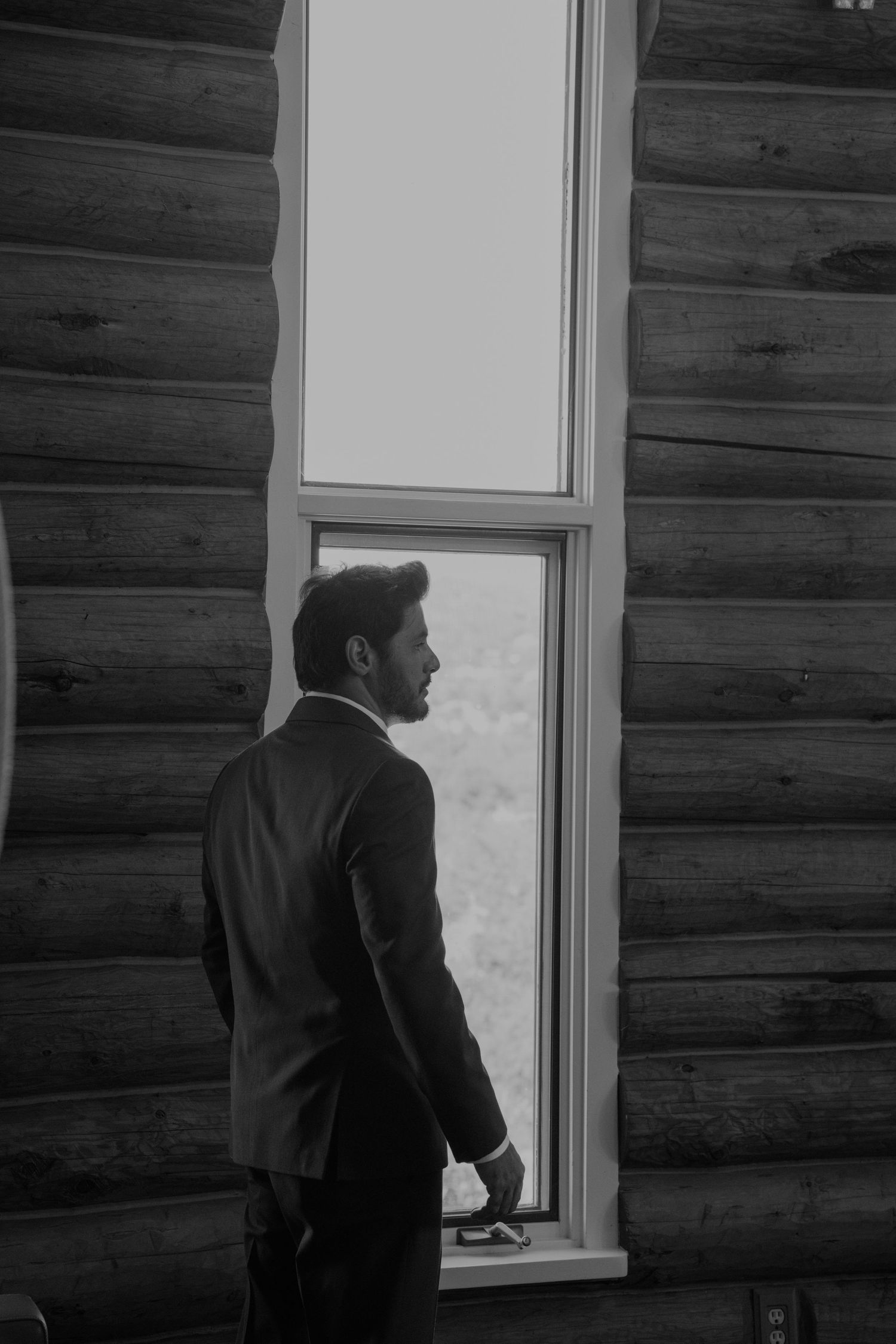 Silhouetted figure looking through window of rustic log cabin.
