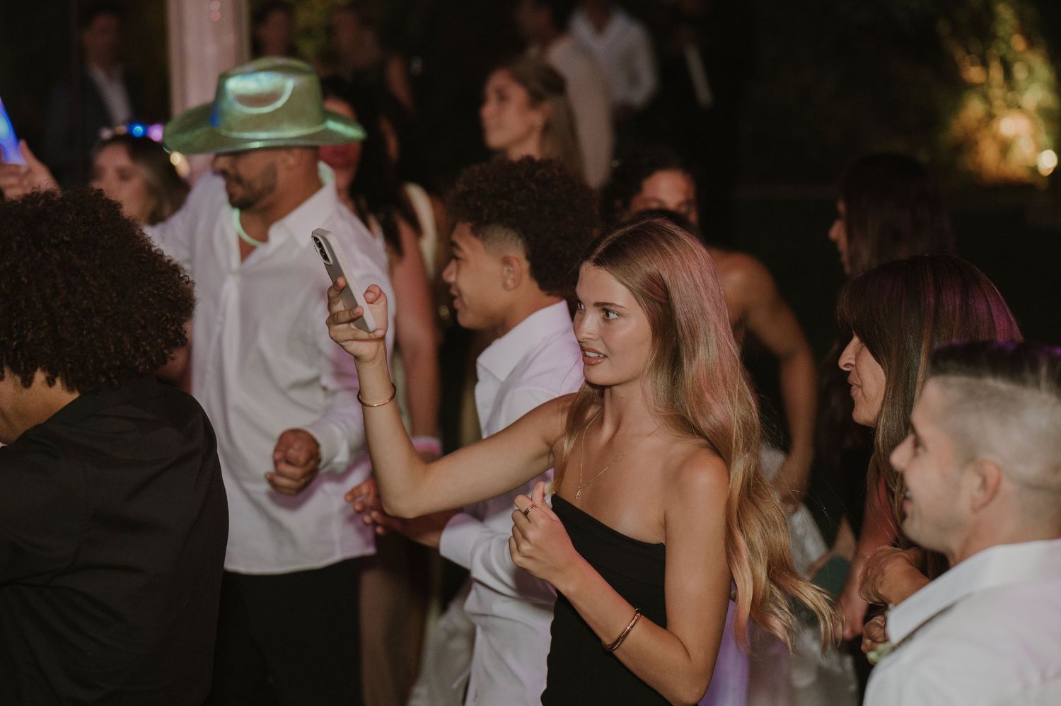 Young woman in black dress dancing with friends at an elegant evening wedding reception.