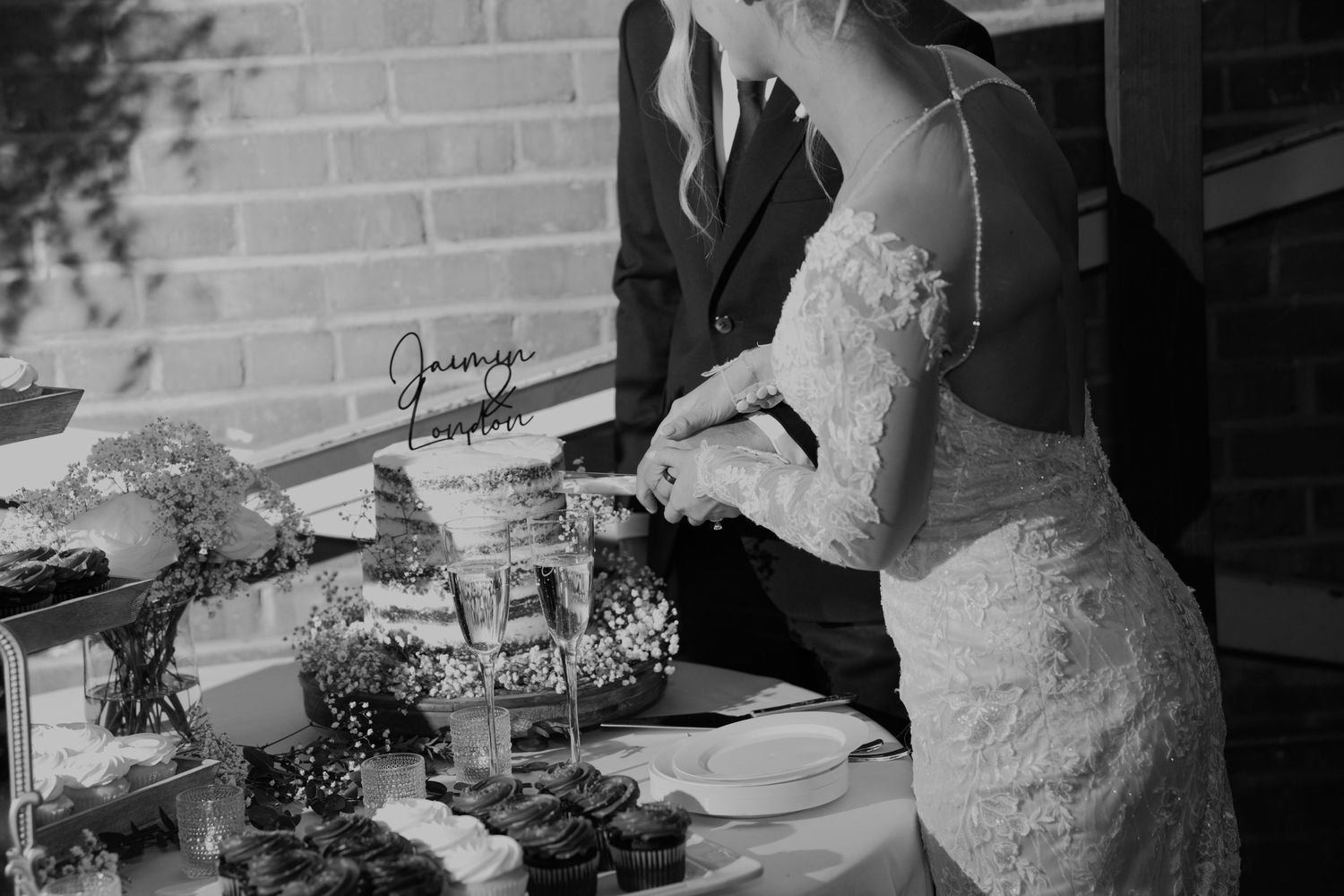 Bride and groom cutting wedding cake at elegant dessert table in black and white photo.