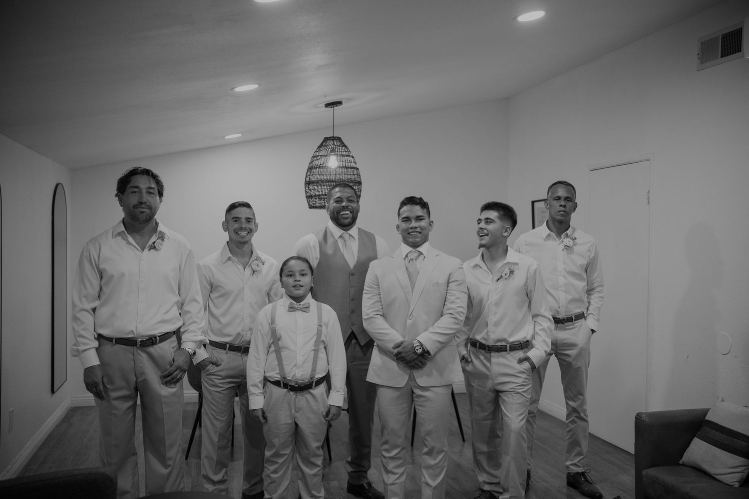 Black and white photo of groom with groomsmen and young ring bearer posing indoors.