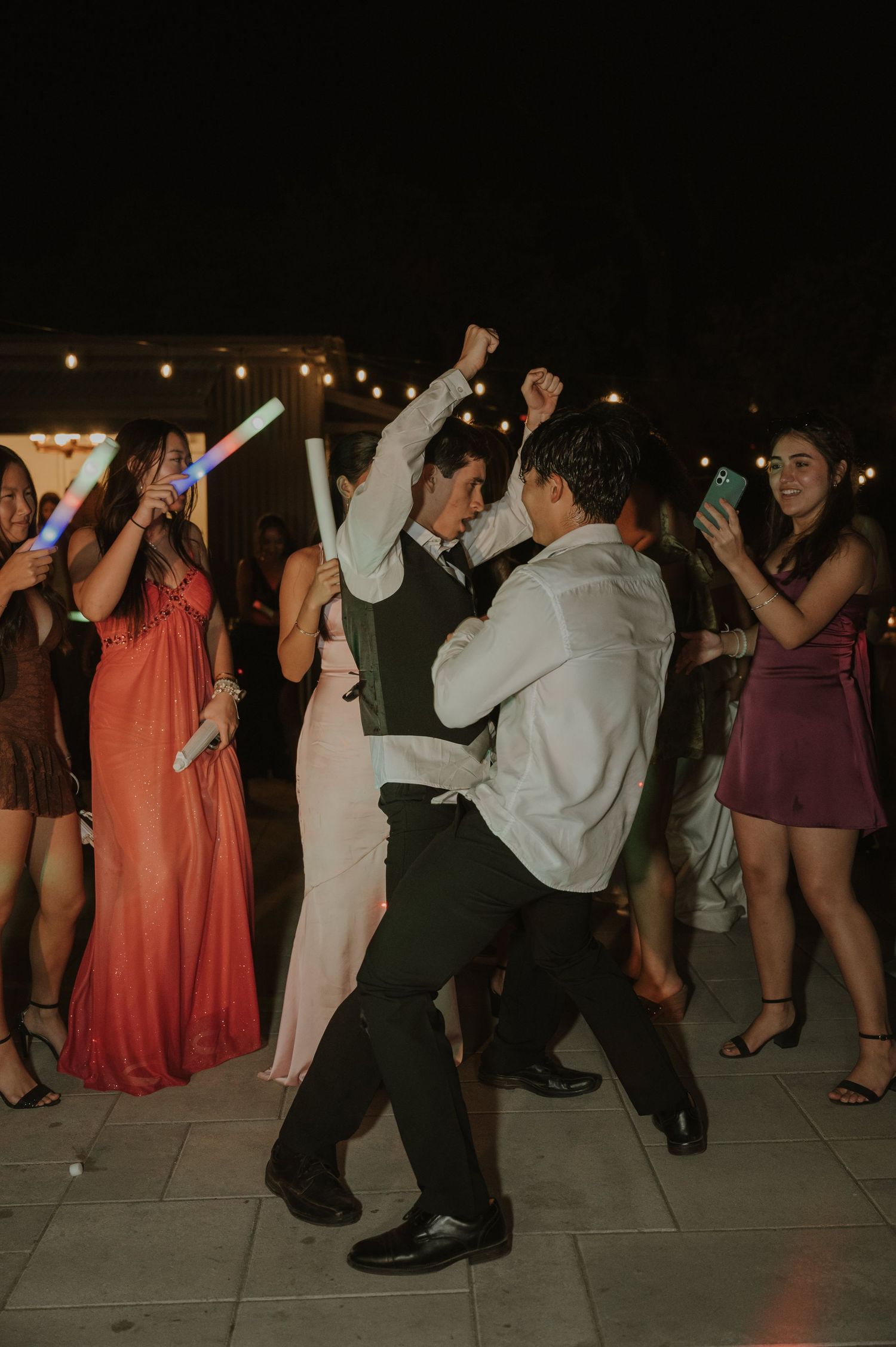 Wedding guests energetically dancing with colorful glow sticks at festive outdoor nighttime reception.