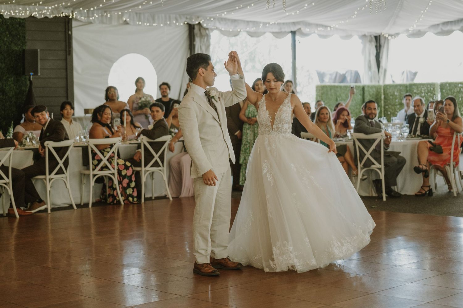 Bride in a lace ballgown and groom in white suit share a joyful first dance at their wedding reception.