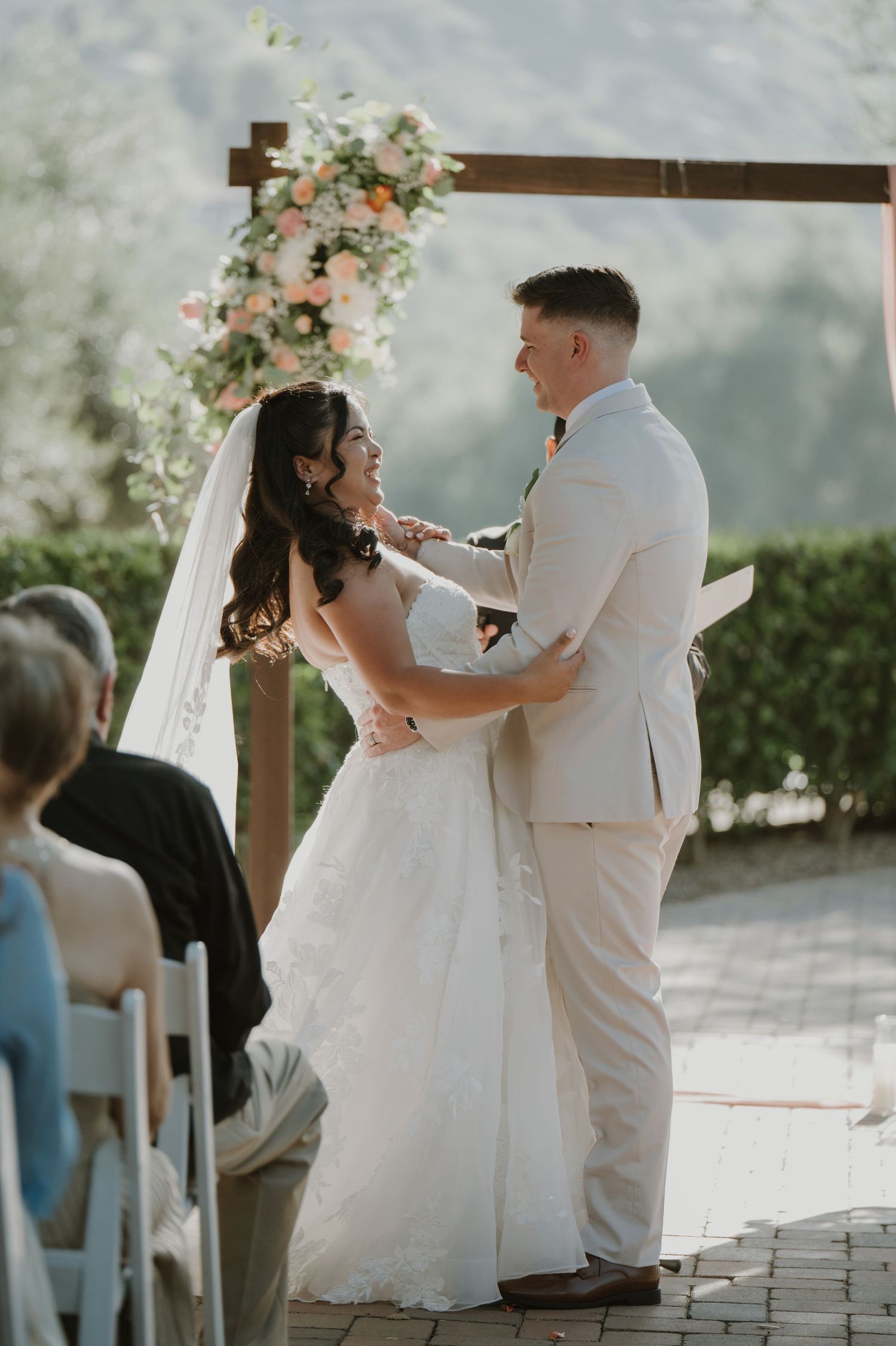 Bride and groom share a joyful moment at the altar under a floral arch at an outdoor wedding.