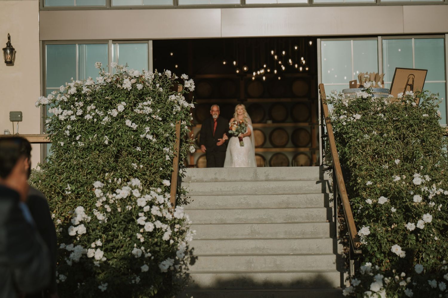 Wedding venue entrance decorated with white roses and string lights at dusk.