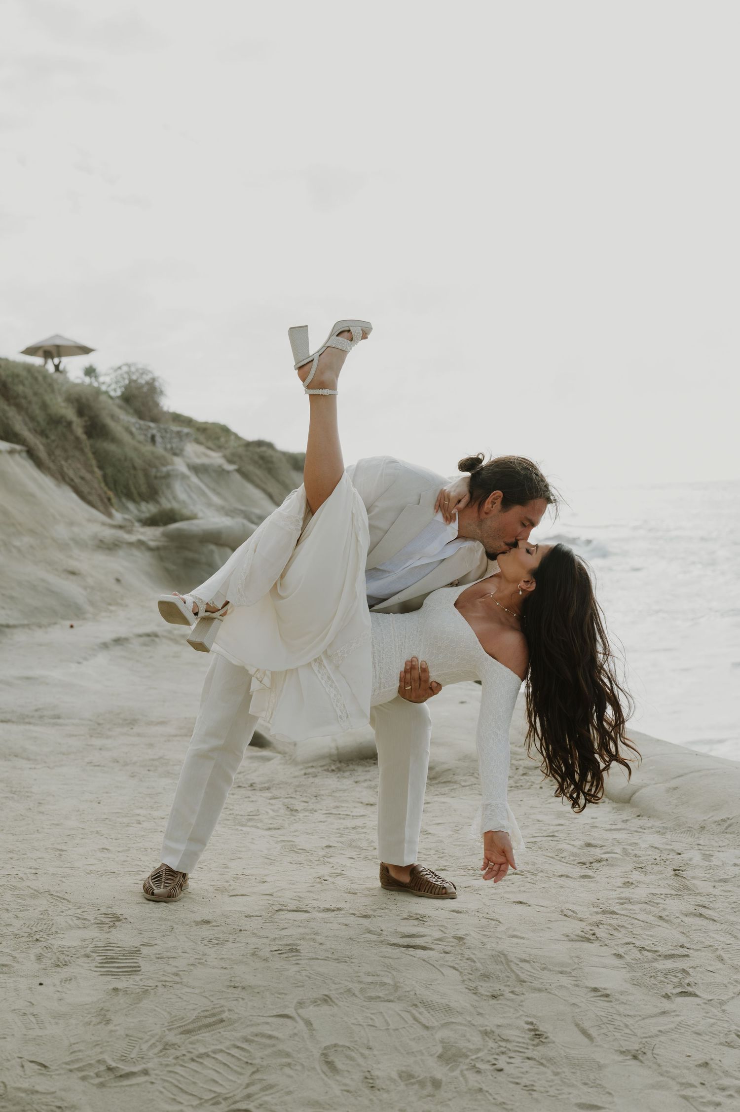 A couple in white performs a dramatic dance dip pose on the beach.