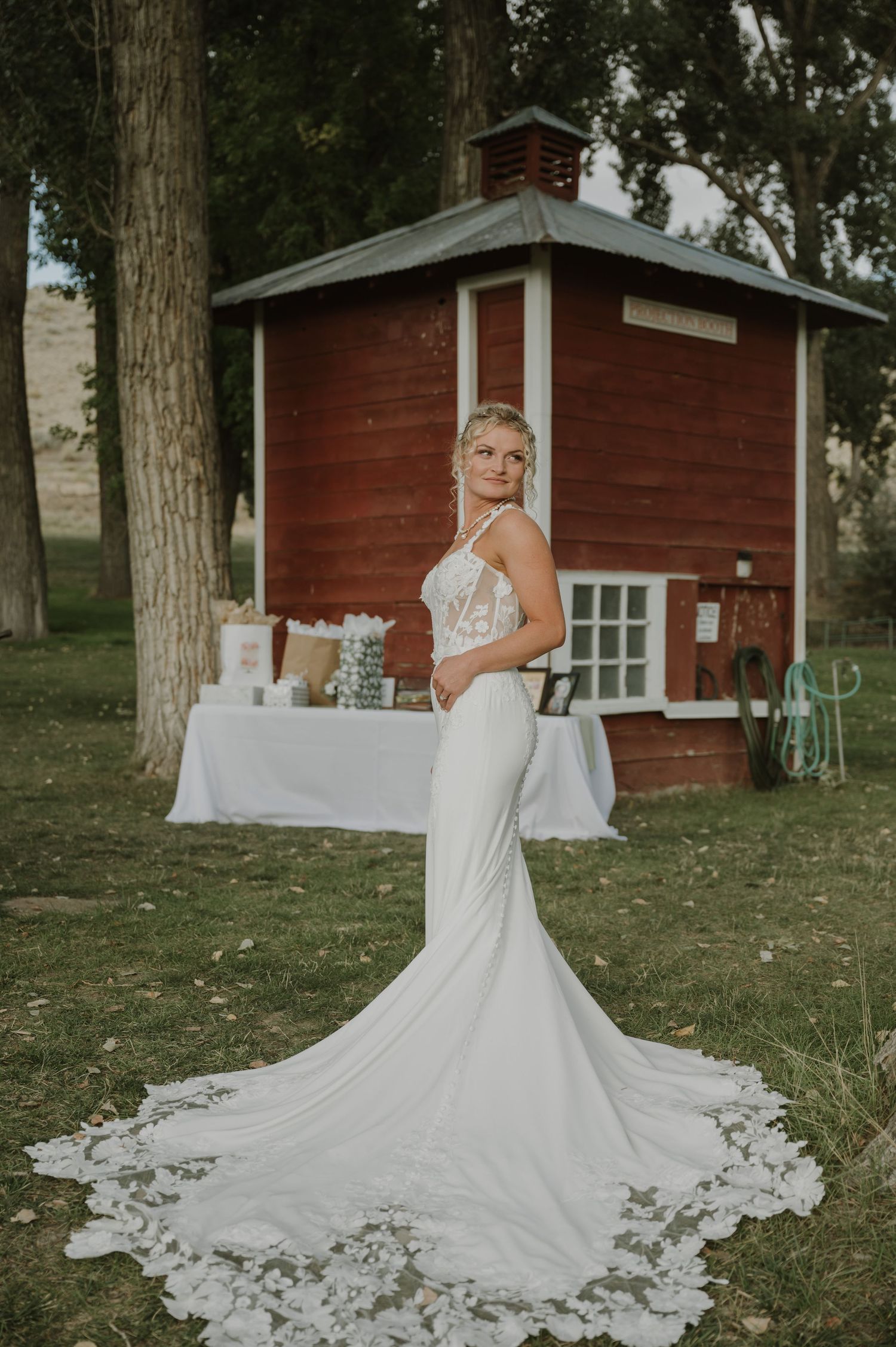 A stunning white wedding dress with a flowing train displayed against a rustic red barn backdrop.