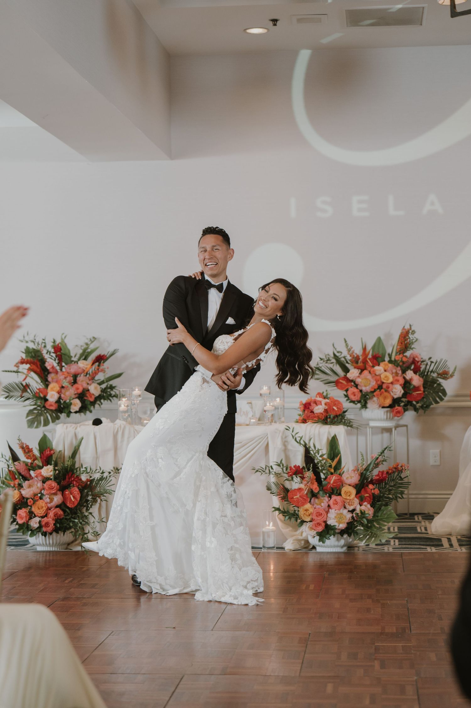 Couple sharing a playful moment during their wedding reception with coral floral decorations.