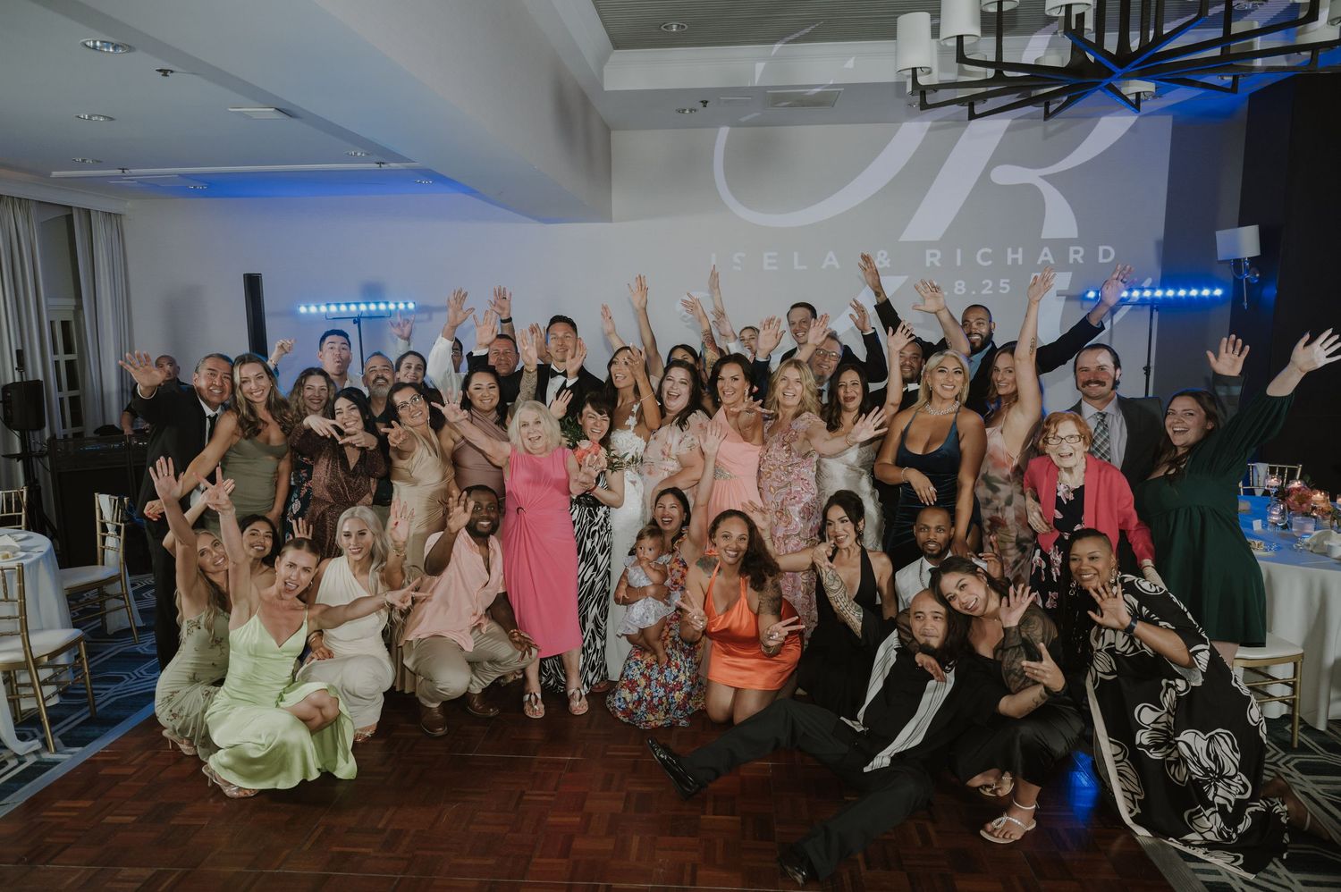 Large group of wedding guests posing together with raised arms in celebration.