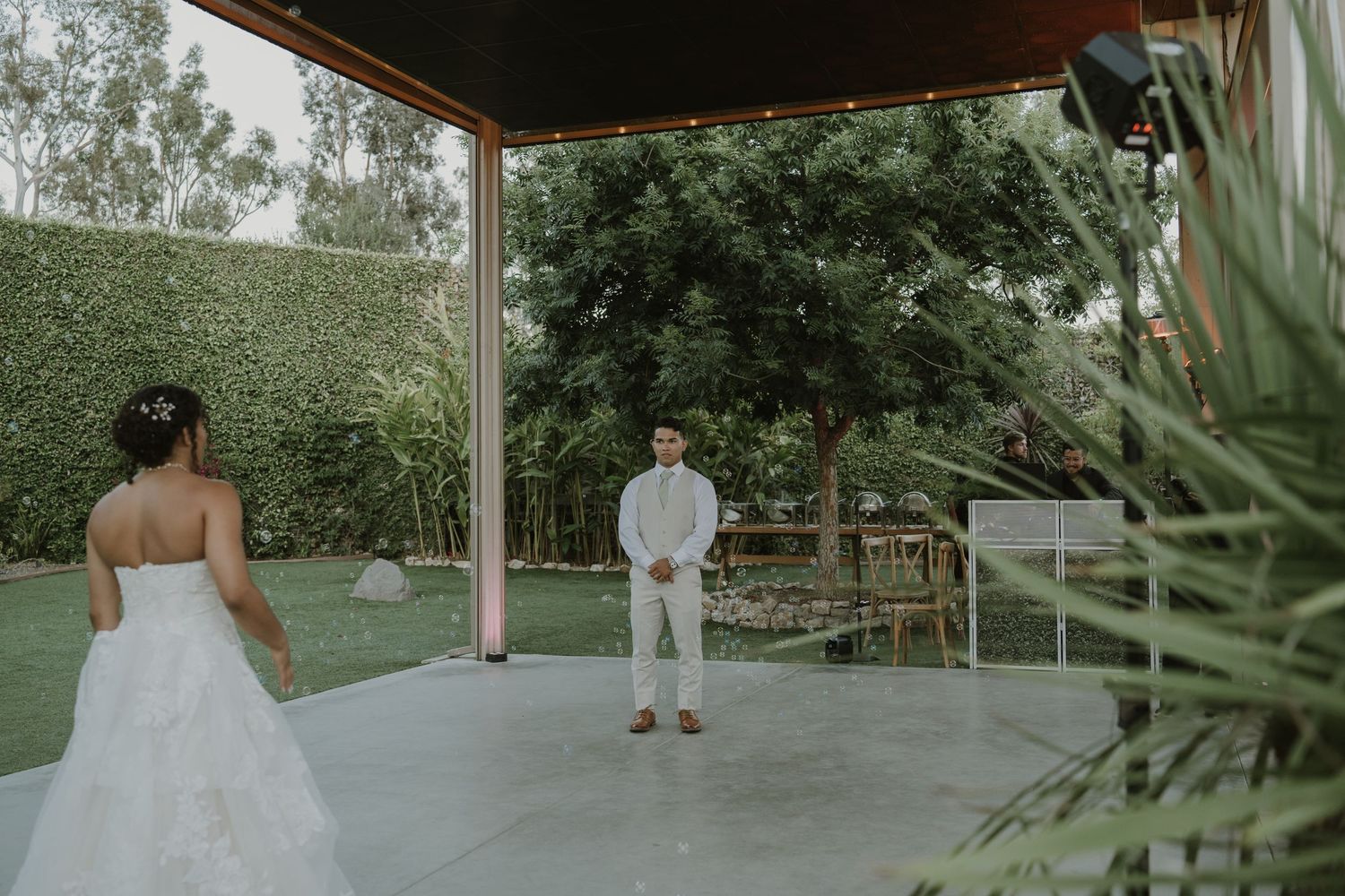 Bride in white gown approaches groom in white suit during first look at outdoor wedding venue.