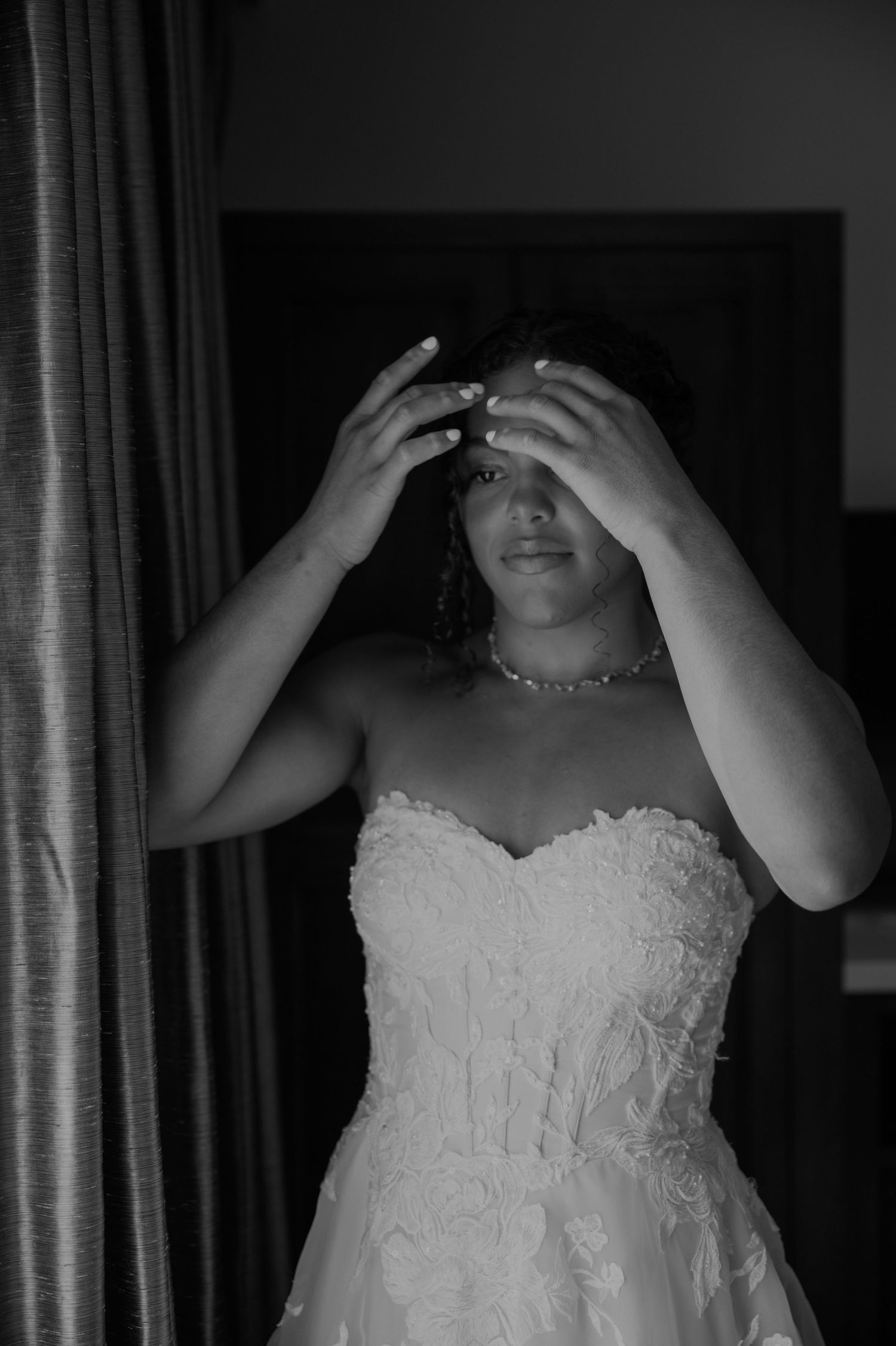 Black and white portrait of a bride in a strapless lace wedding gown touching her hair.