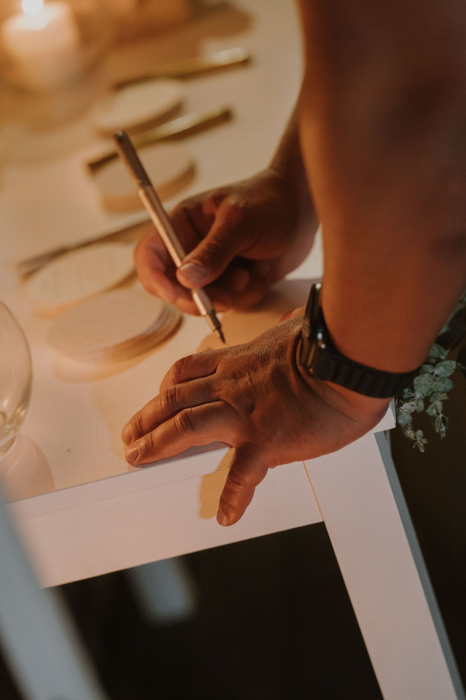 Close-up of groom signing wedding guest book with pen while wearing a watch at elegant reception table.
