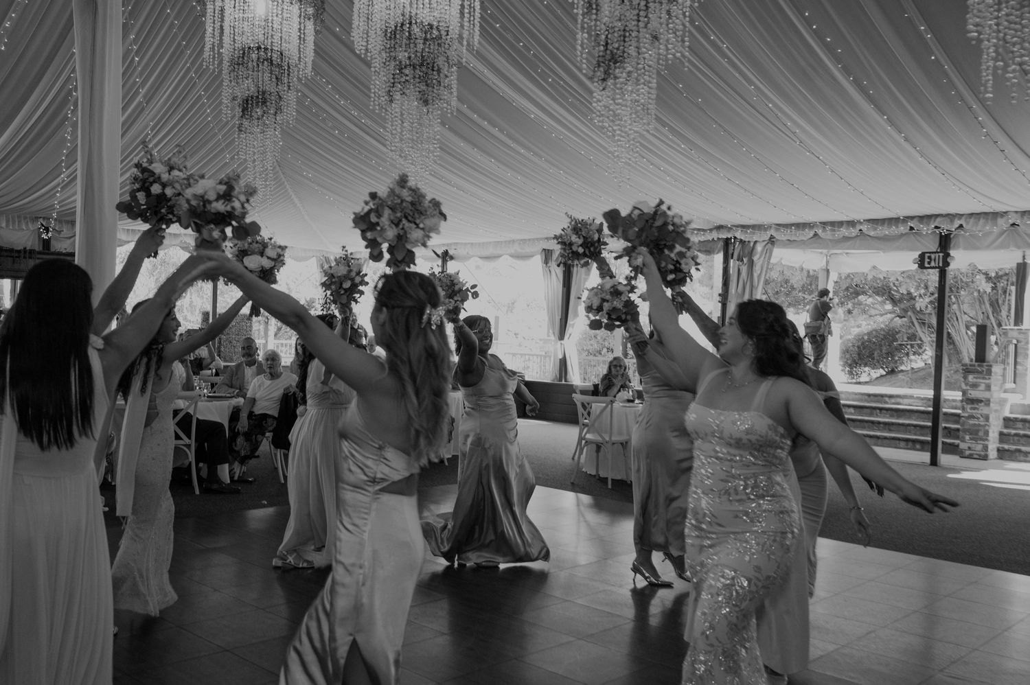 Black and white photo of bridesmaids dancing and raising bouquets on a wedding reception dance floor.