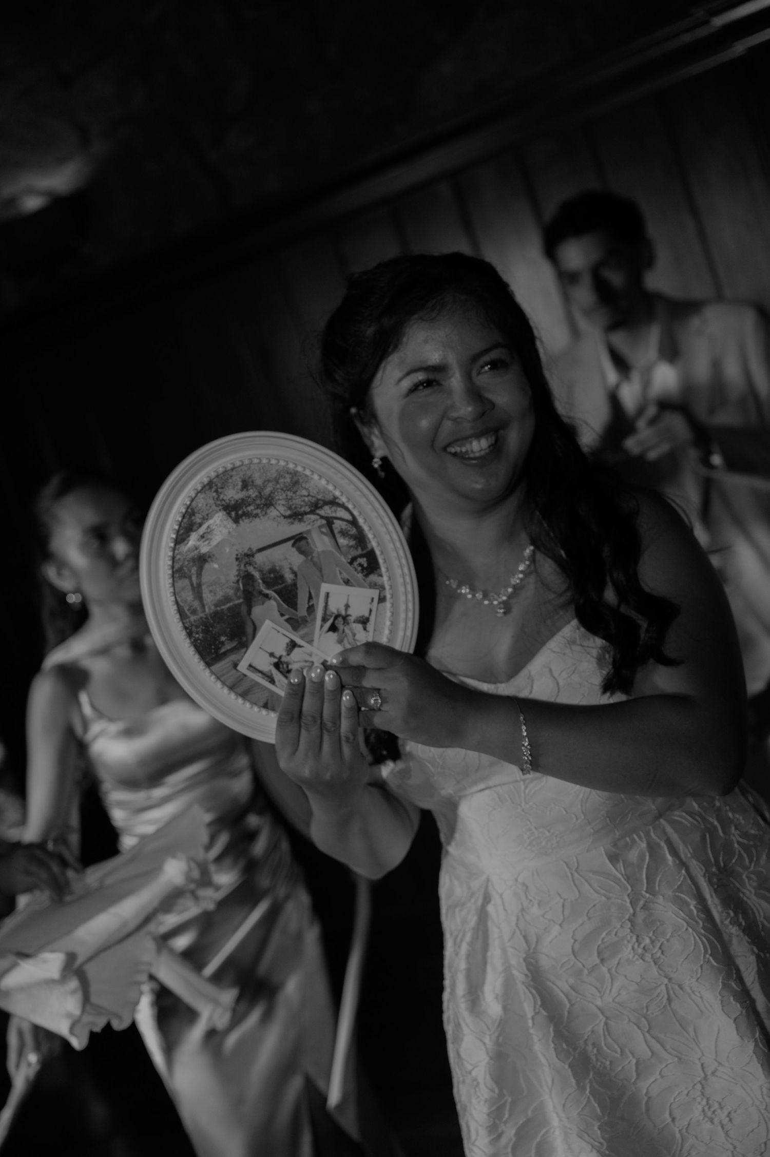 Black and white photo of a smiling bride holding a decorative plate with photos at her wedding.