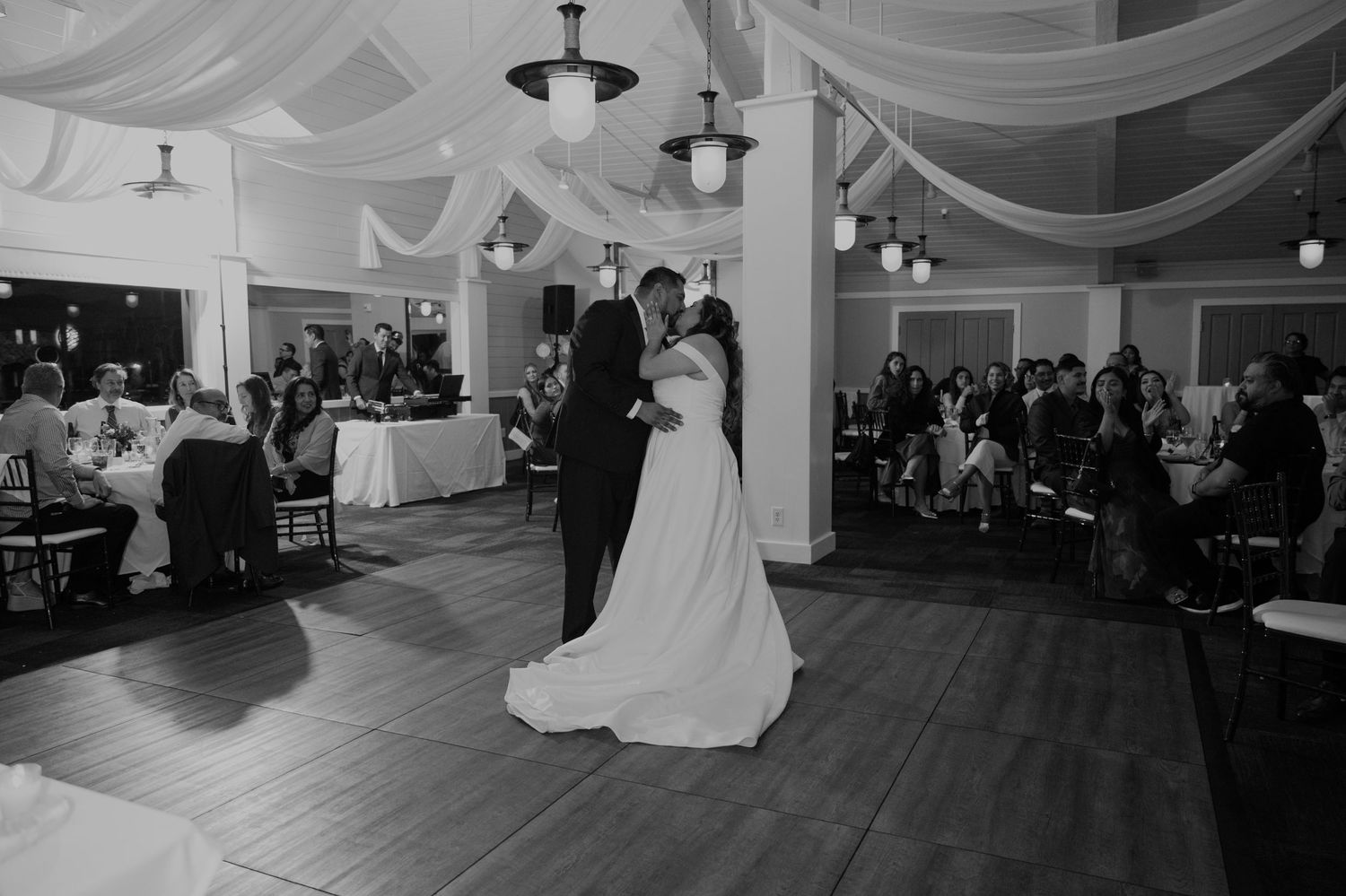 Bride and groom share their first dance in a beautifully decorated ballroom with draped white fabric ceiling.