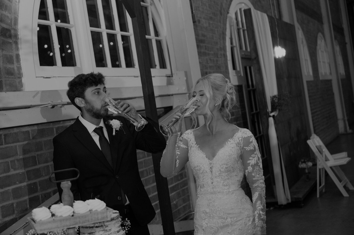 Bride and groom toasting with champagne glasses at their wedding reception in a brick venue.