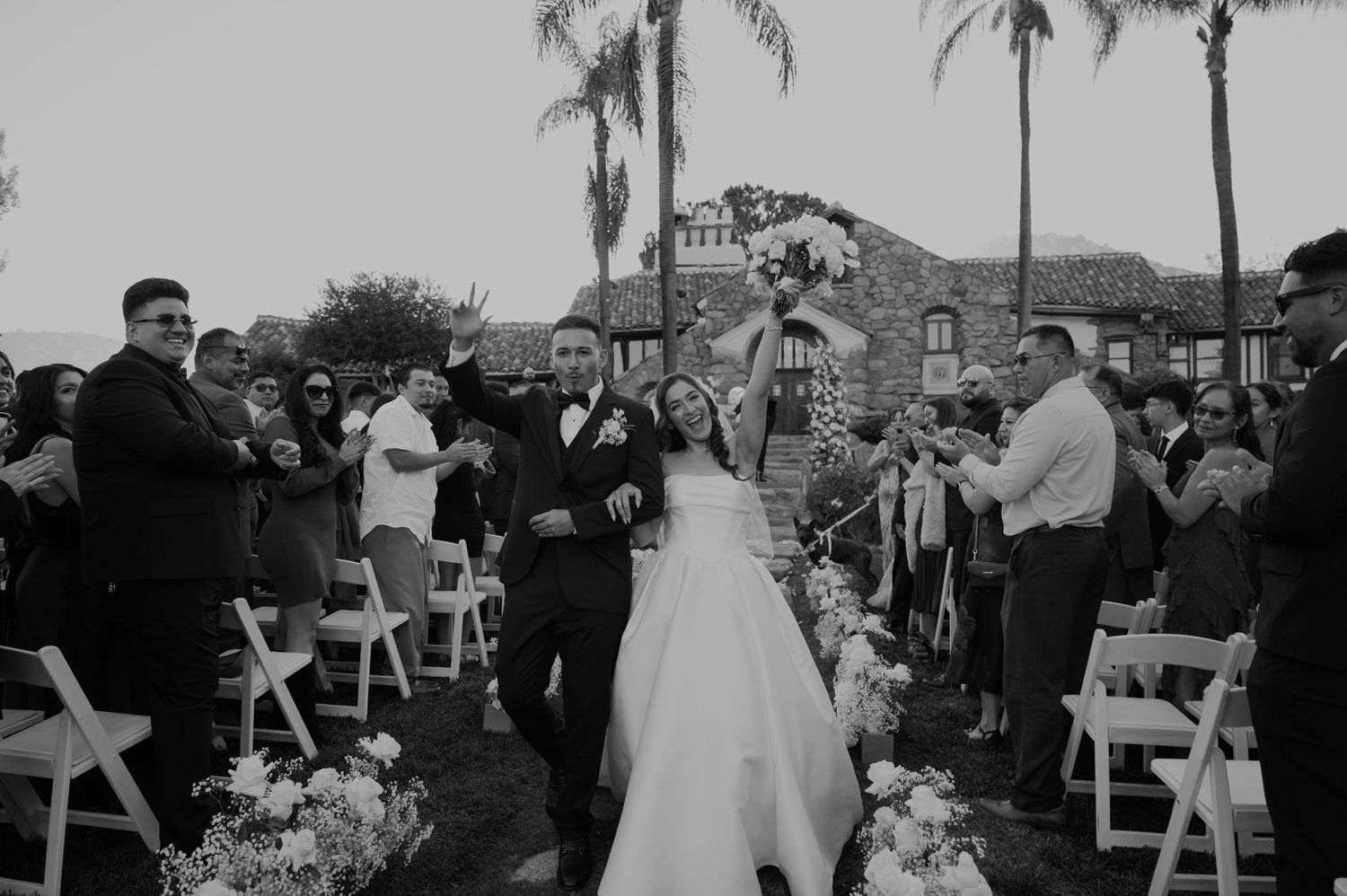 Wedding ceremony setup at a vineyard with white chairs and palm trees in the background.