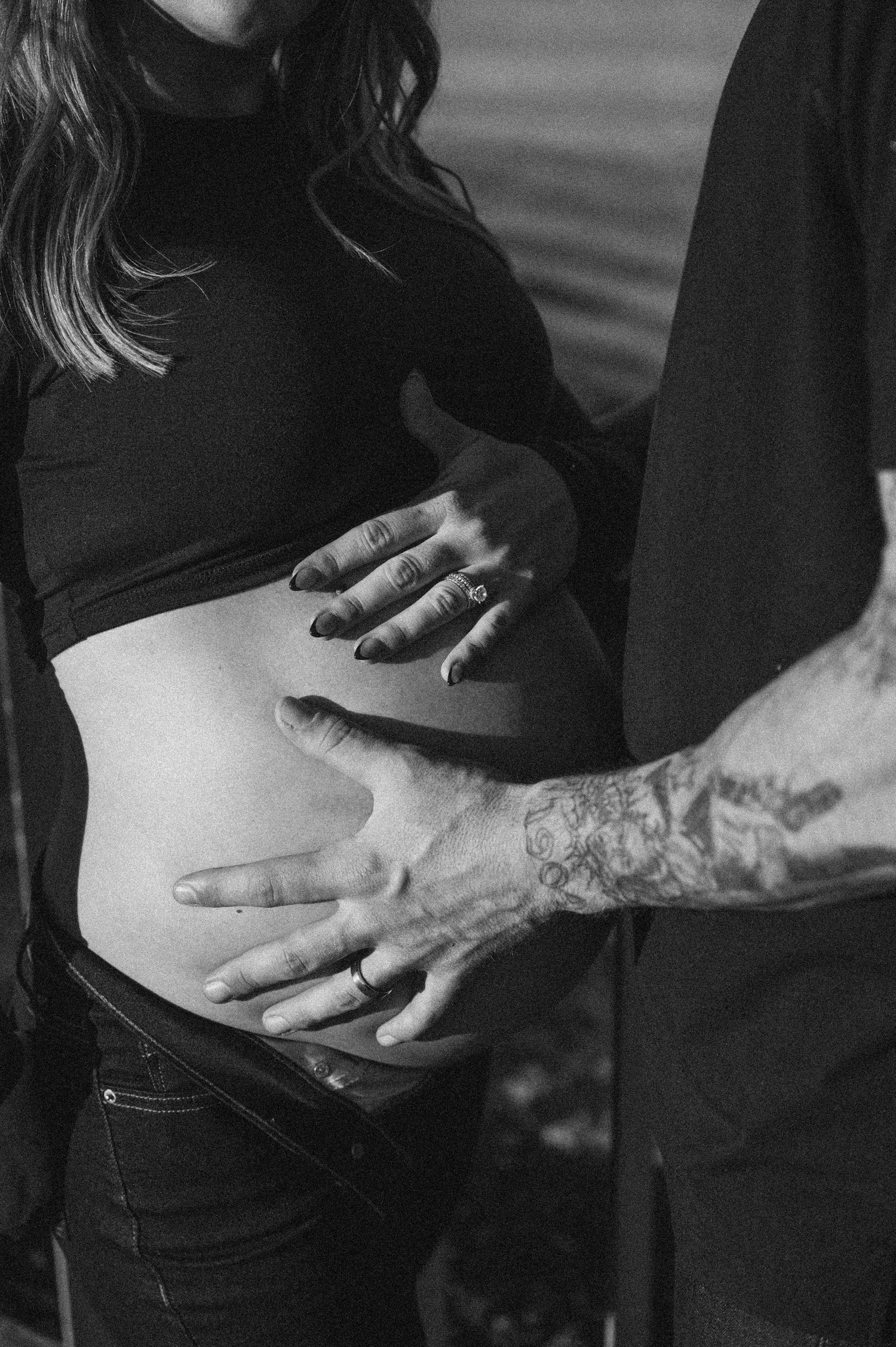 Close-up of hands gently cradling a pregnant belly in black and white.