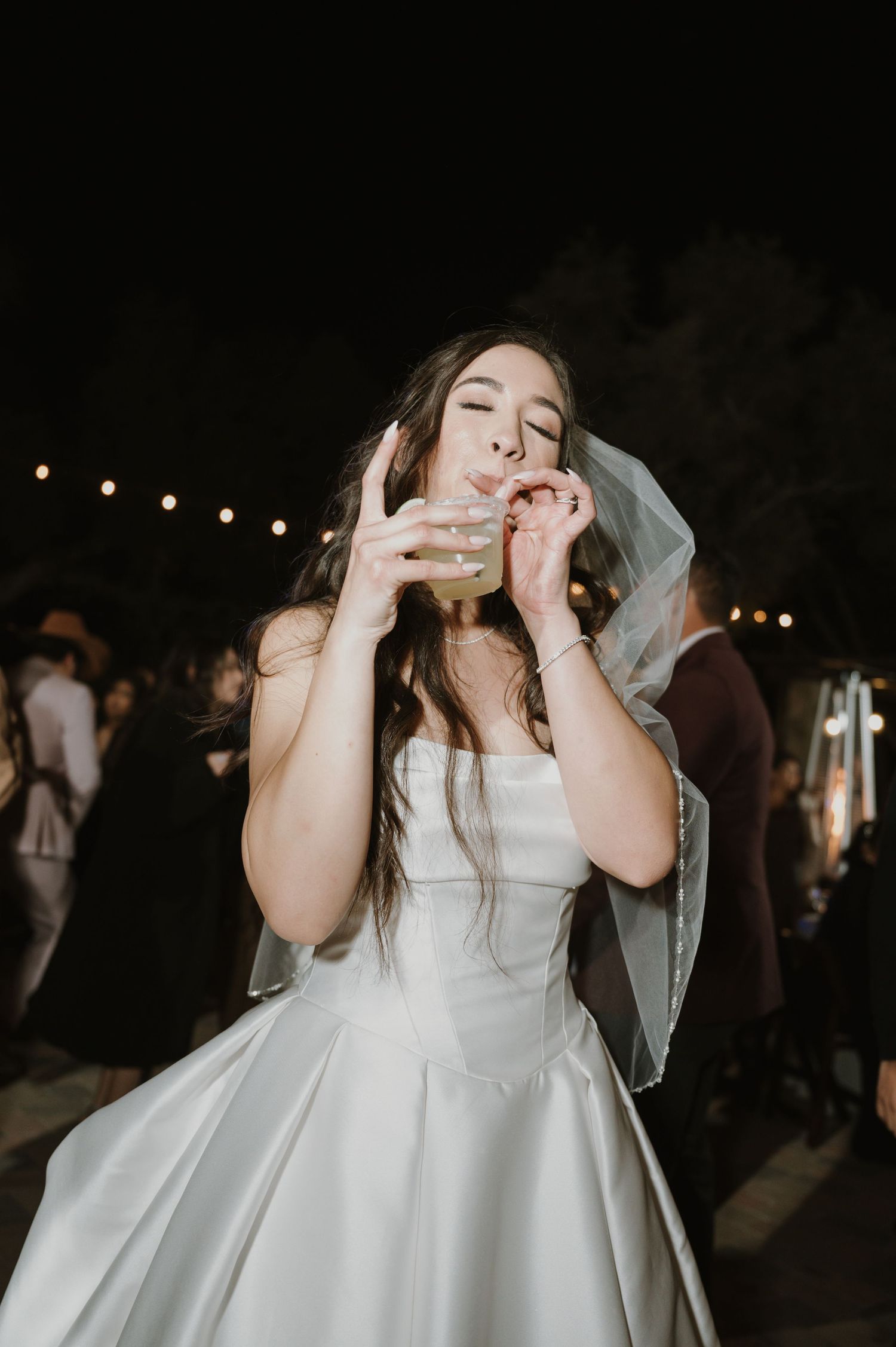 Bride in white dress dancing joyfully at outdoor wedding reception.