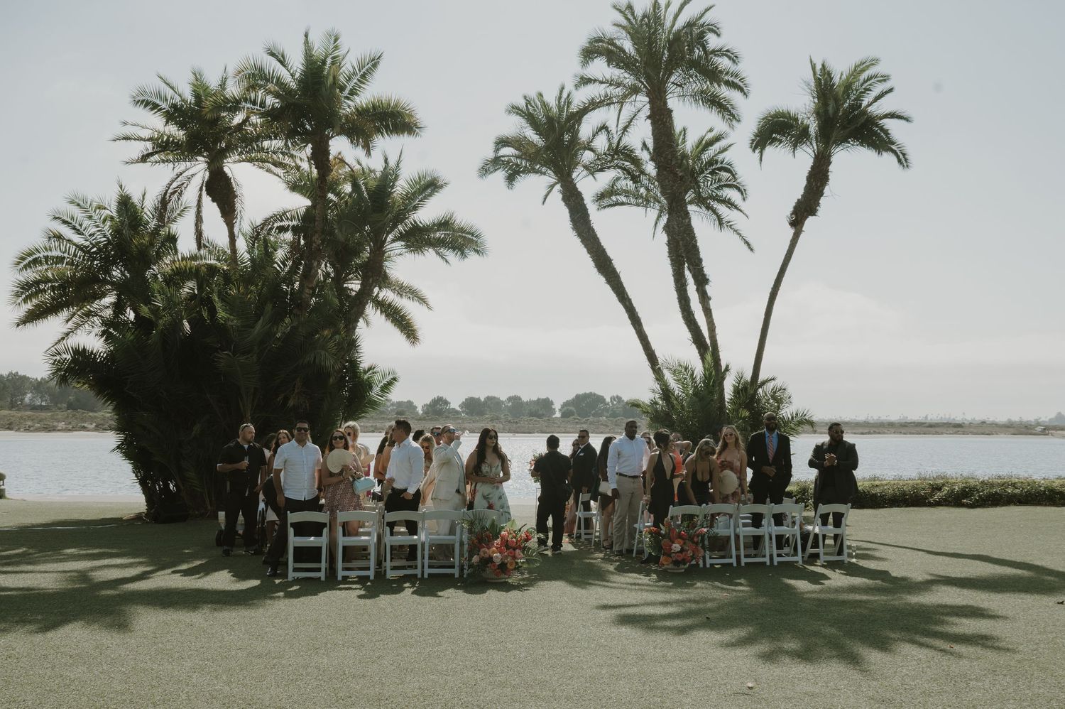 Panoramic view of a beachside wedding ceremony with palm trees and seated guests.