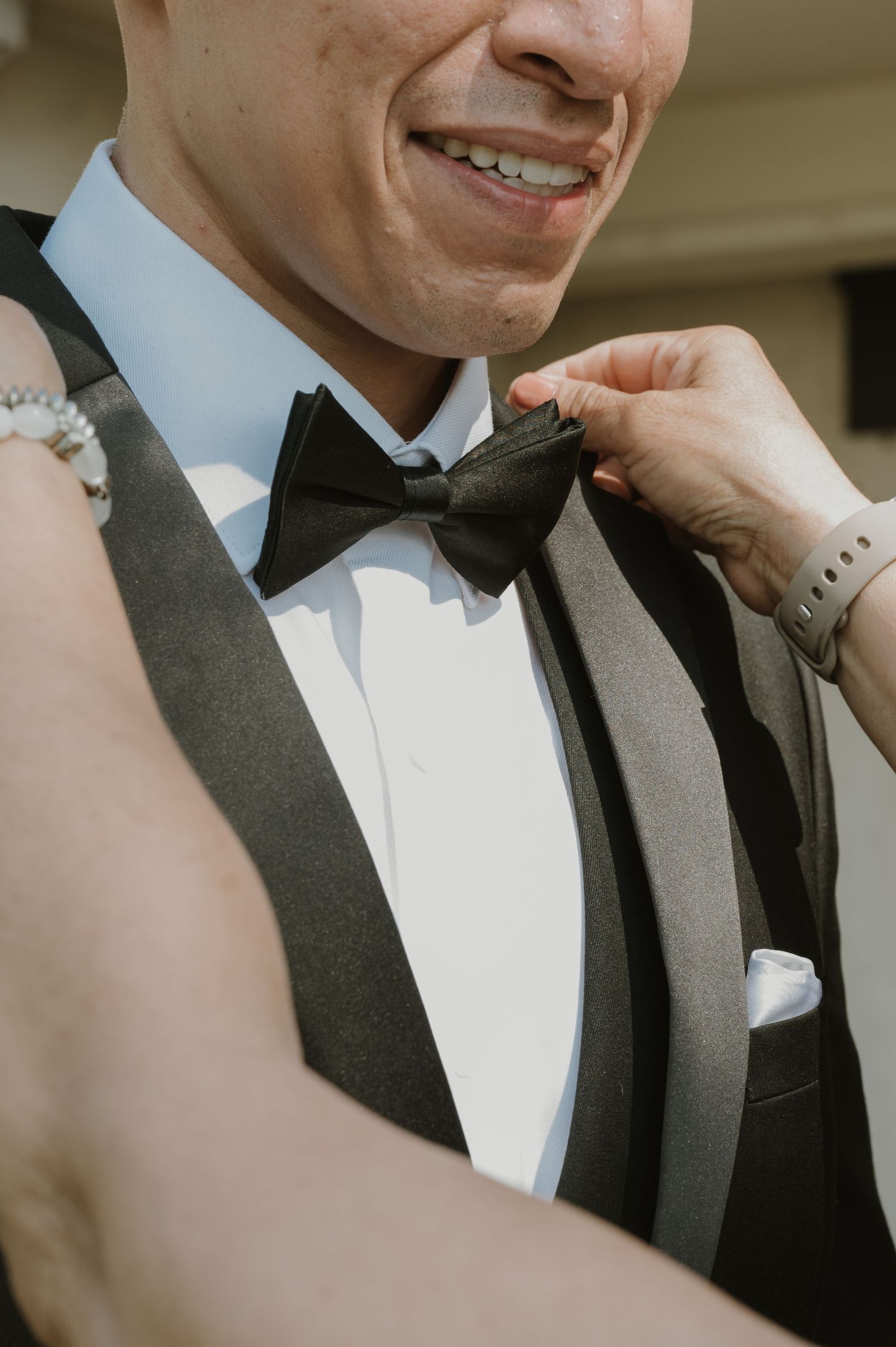 Close-up shot of hands adjusting black bow tie on formal tuxedo.