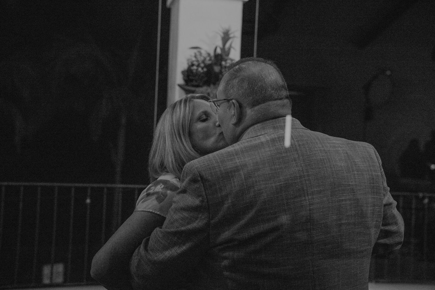 Black and white photo of a tender embrace between a bride and an older man at an outdoor event.