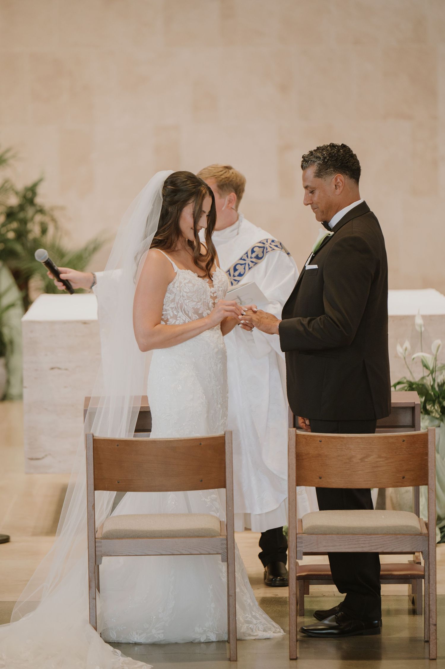 Bride and groom exchange rings during wedding ceremony as officiant presides at church altar.