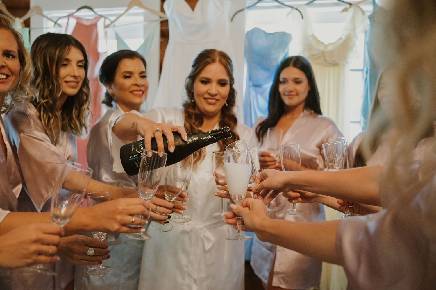 Bride pours champagne for bridesmaids in matching robes during wedding morning preparations.